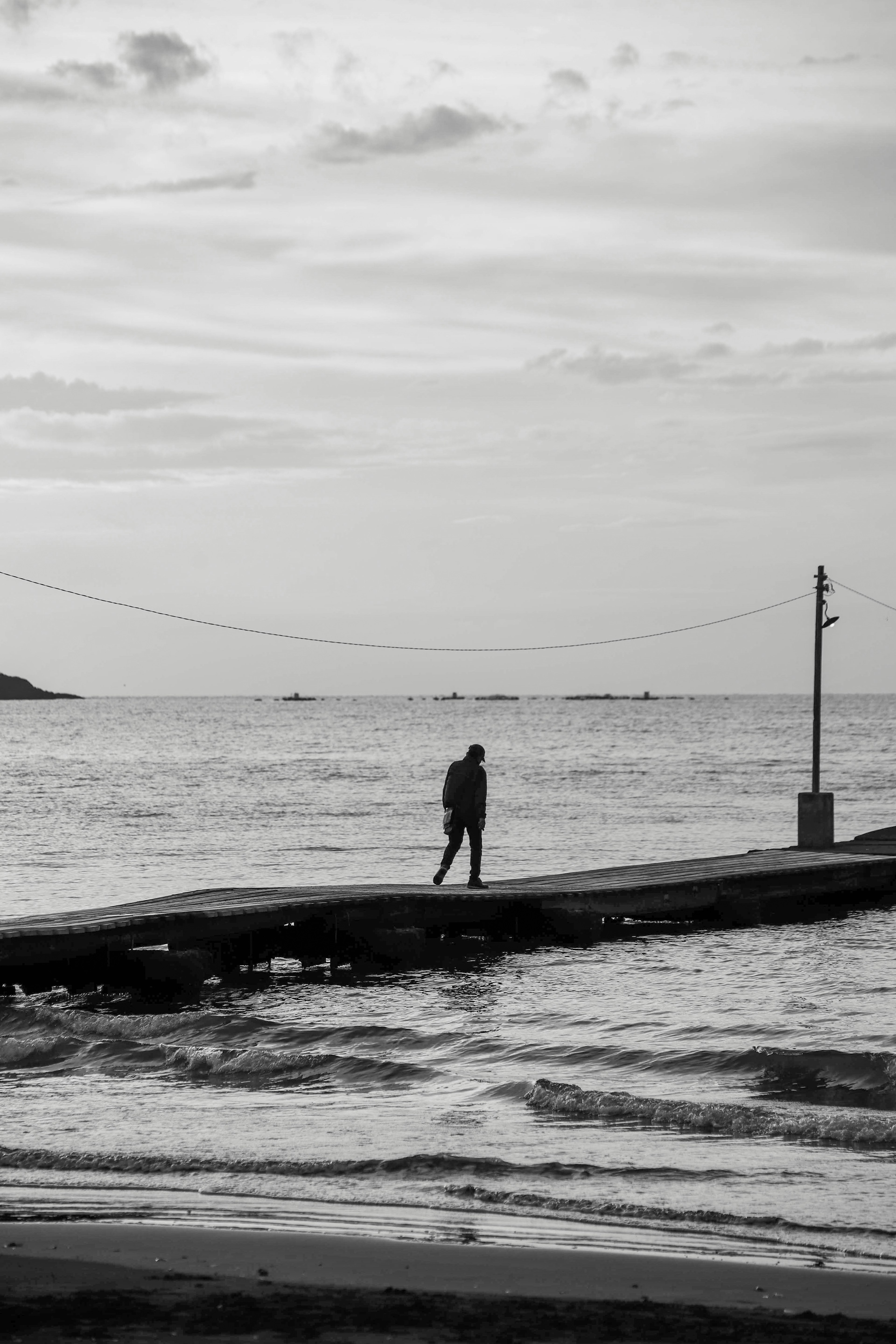 Schwarzweißfoto einer Person, die auf einem Pier am Meer steht