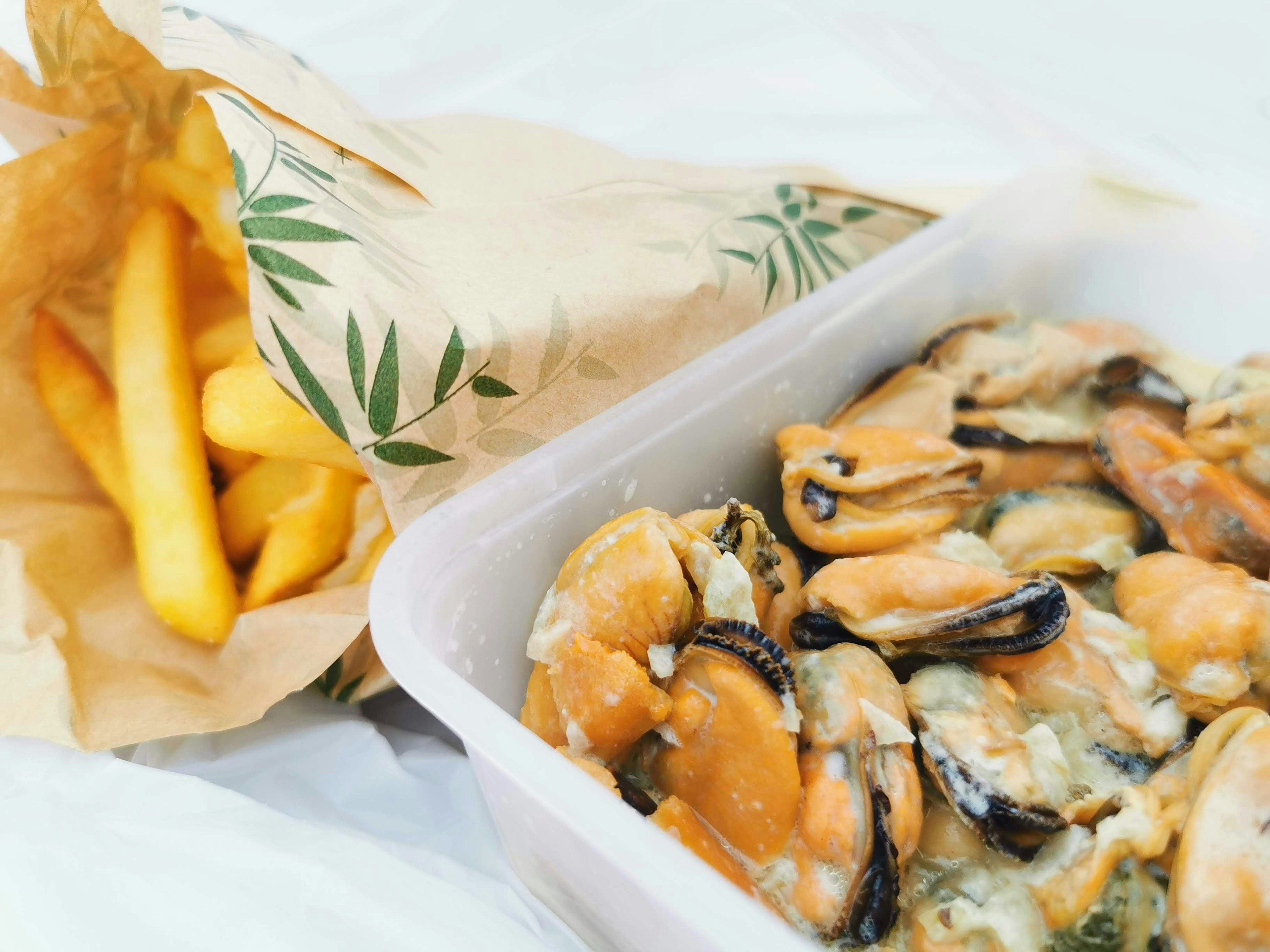 A serving of mussels with French fries in a paper bag