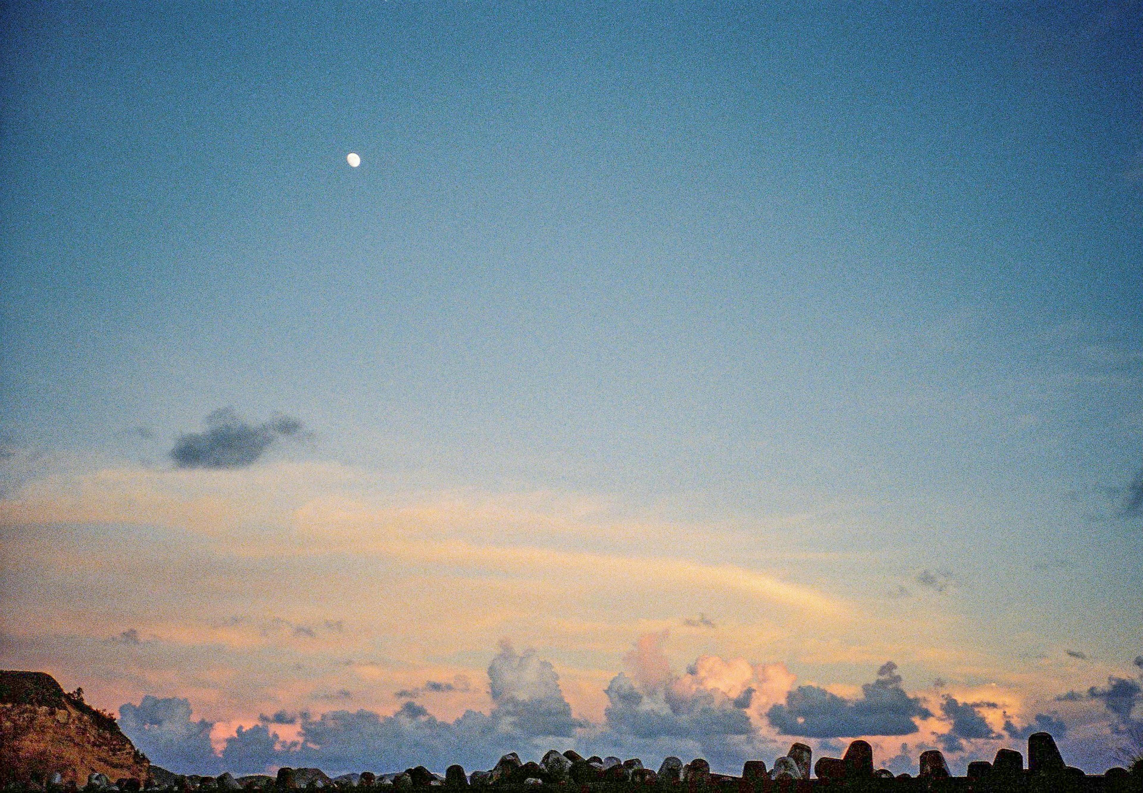 Pemandangan dengan langit biru, awan putih, dan bulan yang terlihat