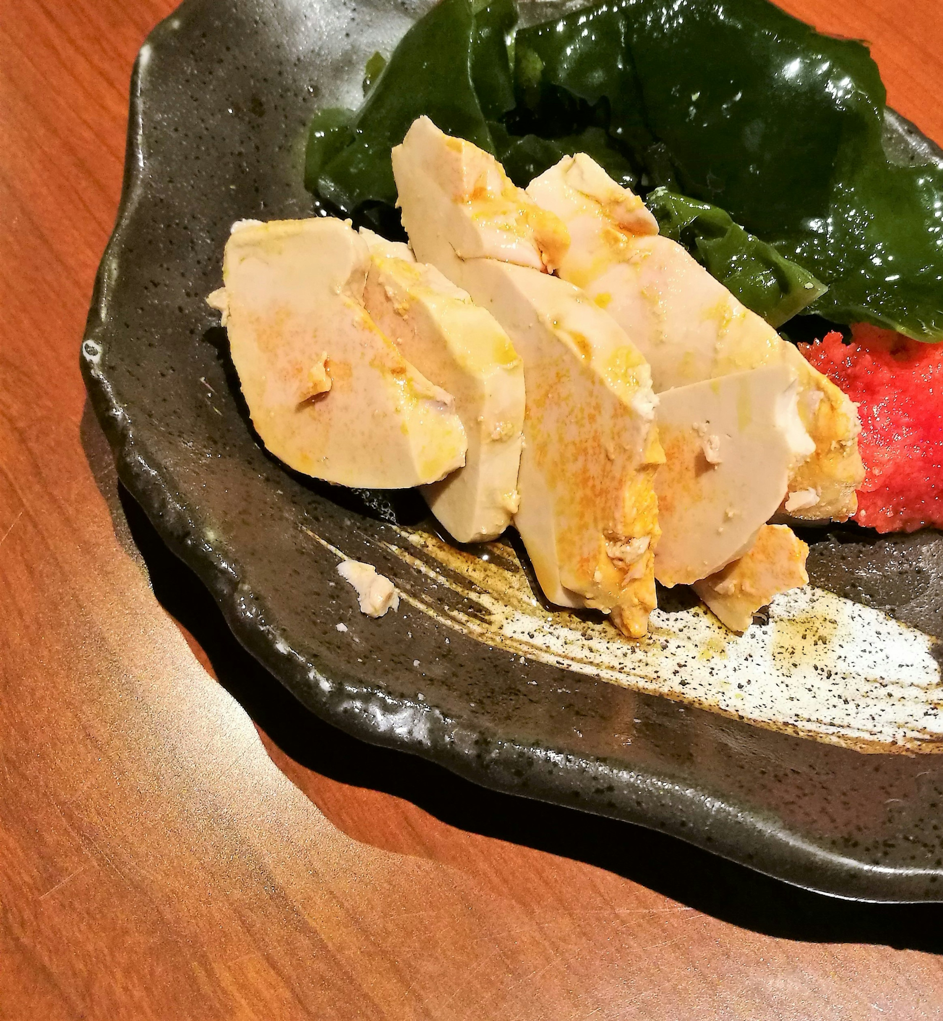 Sliced chicken dish served with seaweed salad on a dark plate