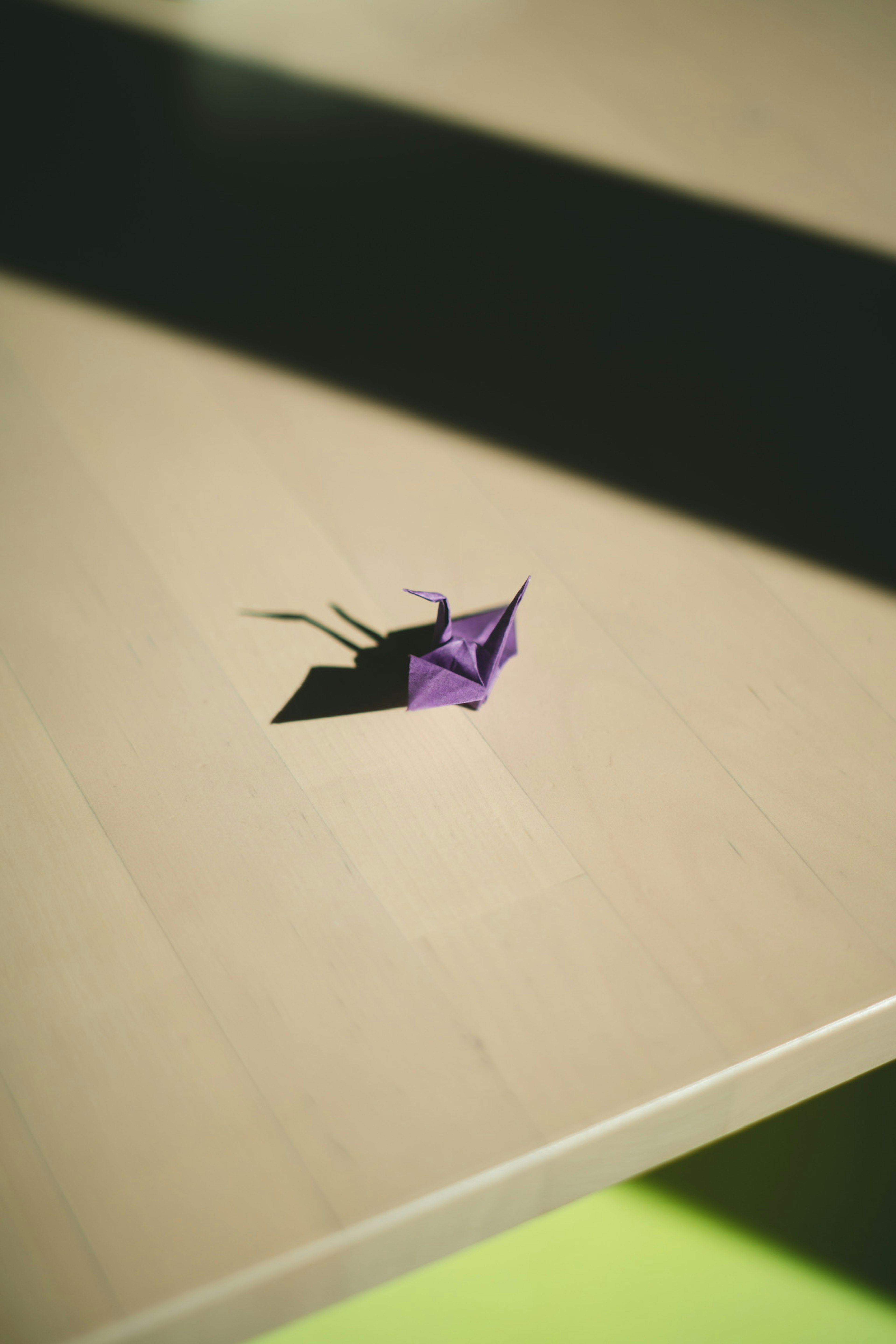 Una grulla de origami púrpura proyectando una sombra sobre una mesa de madera