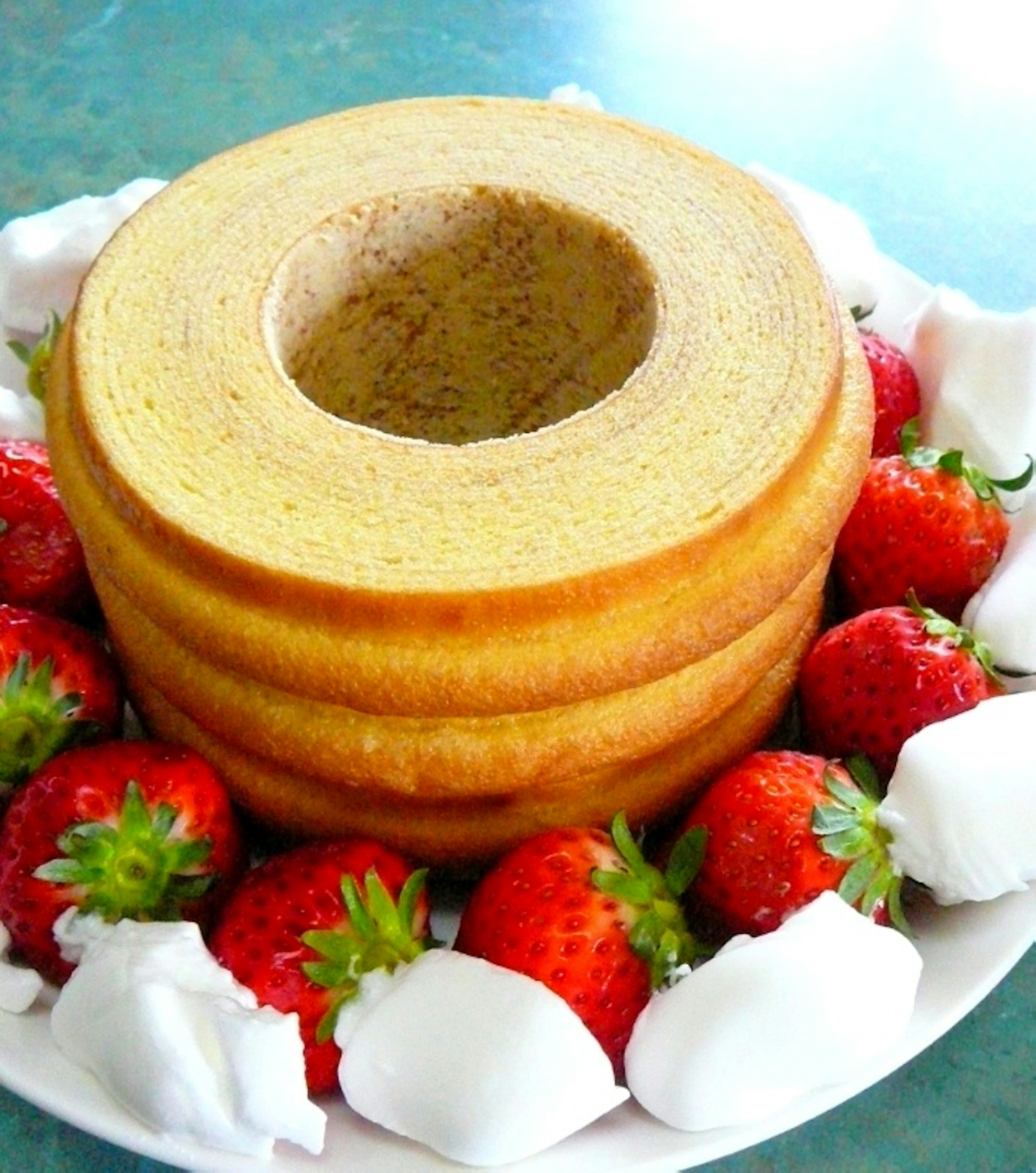 Baumkuchen en capas con un agujero central rodeado de fresas frescas y crema