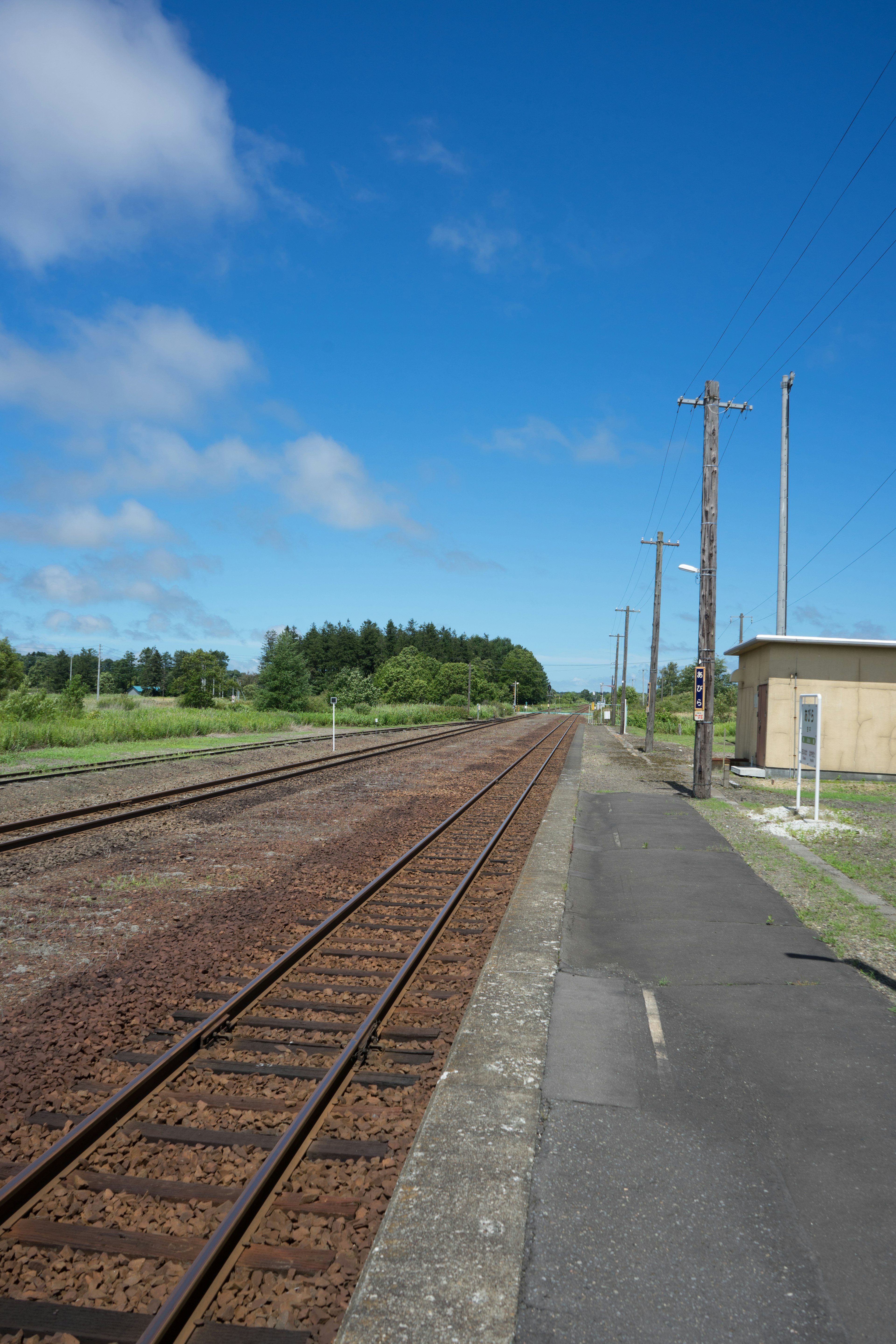 Railway tracks under a clear blue sky with a paved walkway