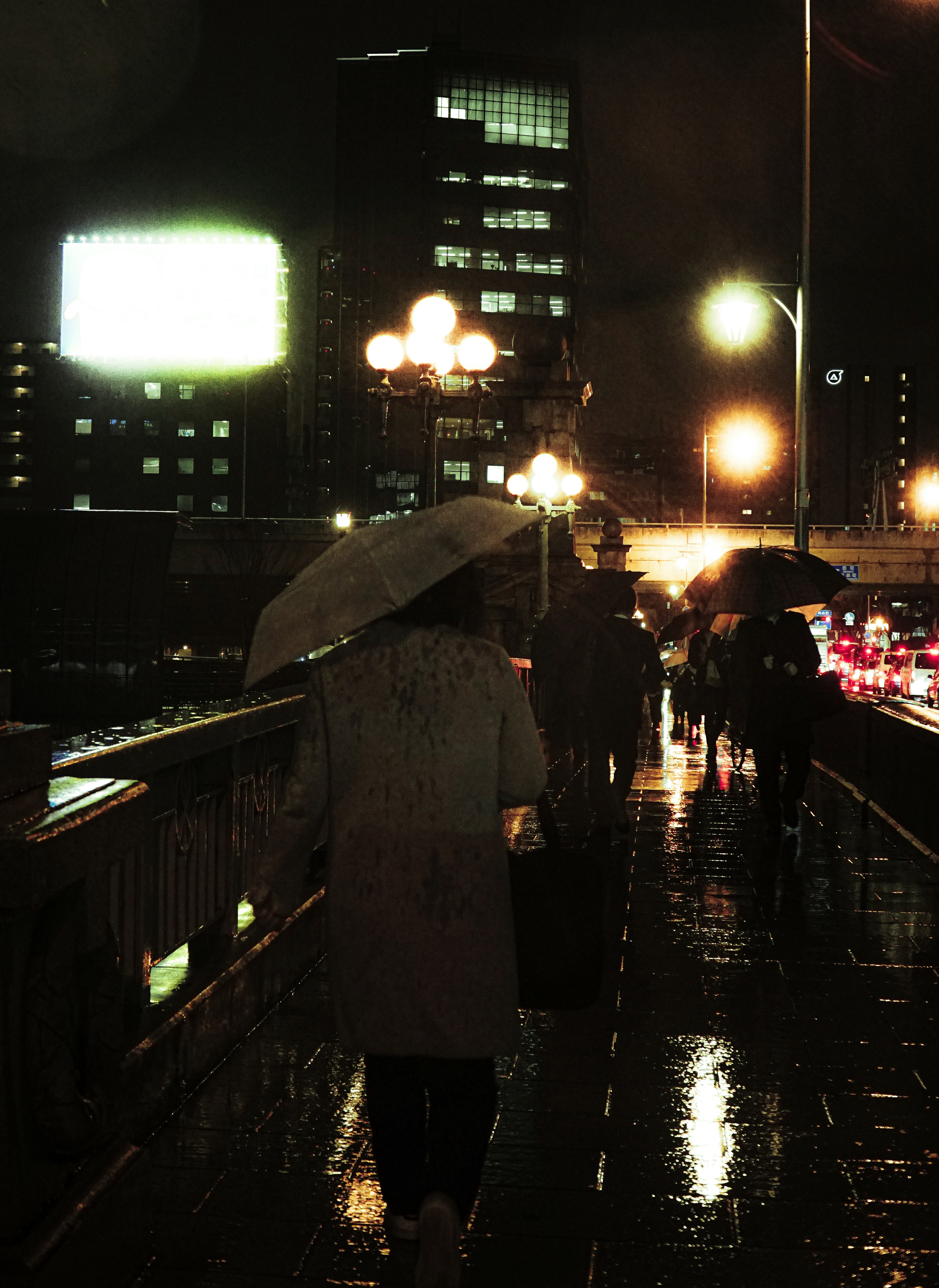 Menschen, die nachts auf einer Brücke mit Regenschirmen auf einer nassen Straße gehen