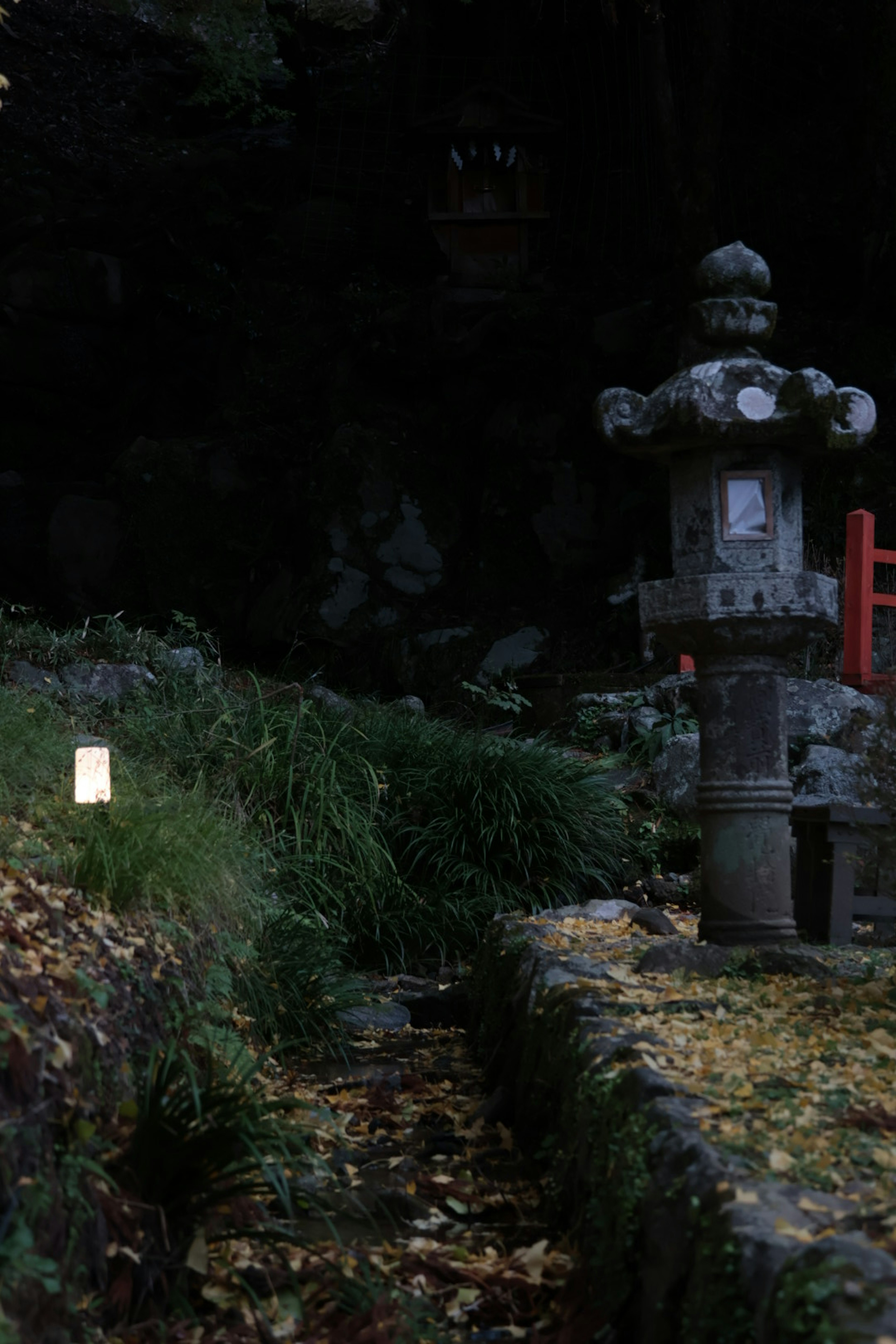 A serene landscape featuring a stone lantern and lush greenery in a dark setting