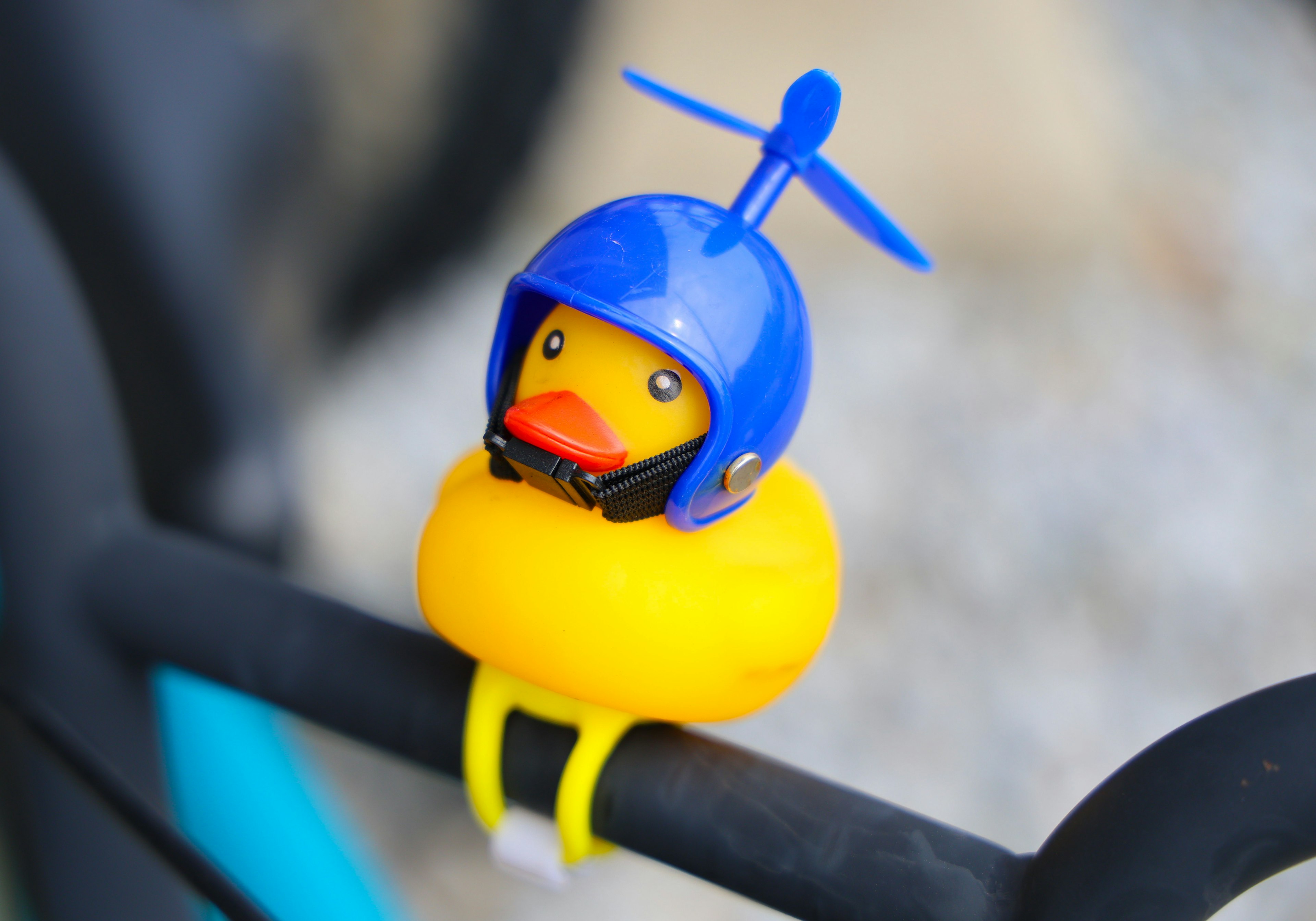 Un pato de goma amarillo con un casco azul está posado en el manillar de una bicicleta