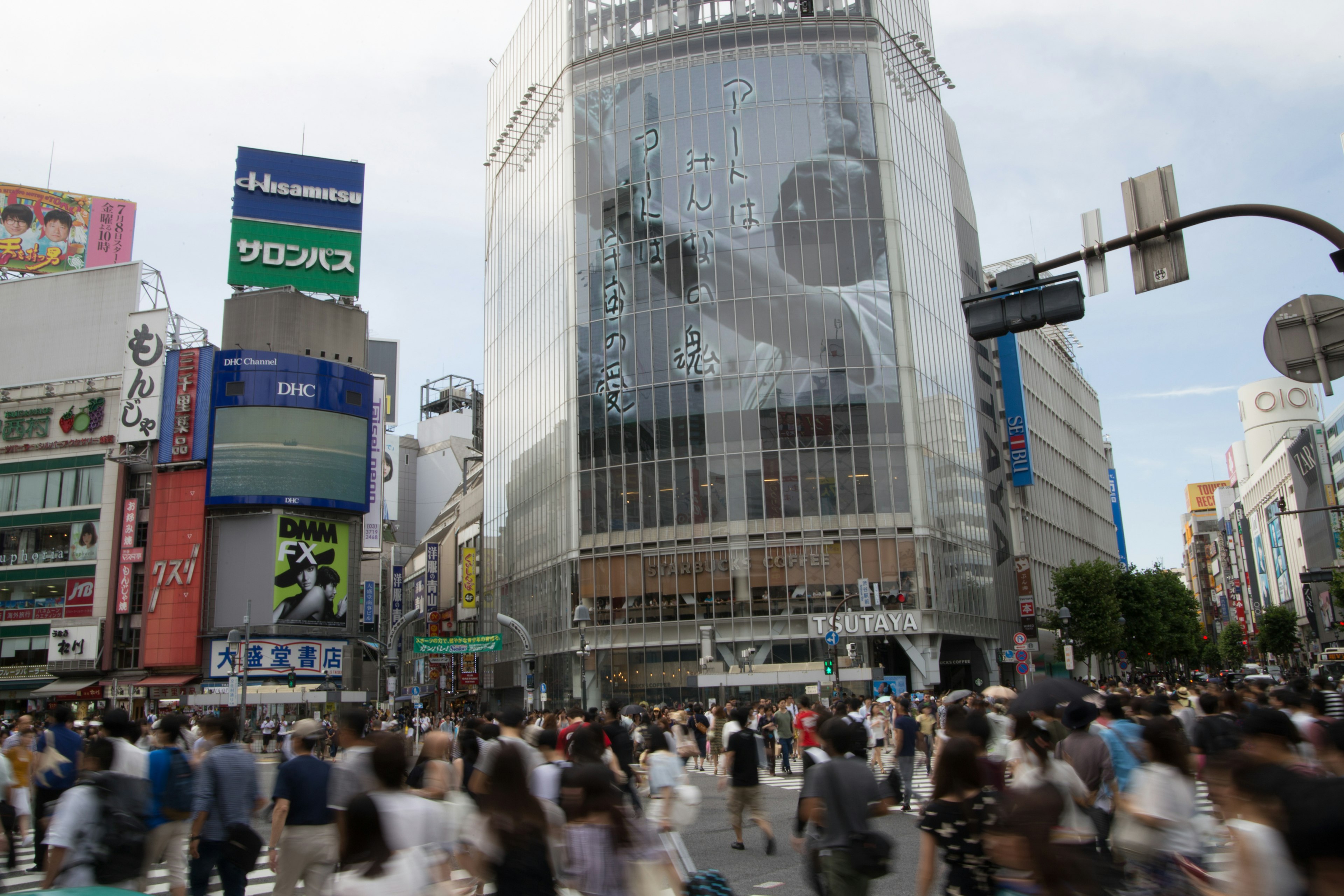 Intersección concurrida de Shibuya con multitudes y un gran edificio que refleja anuncios