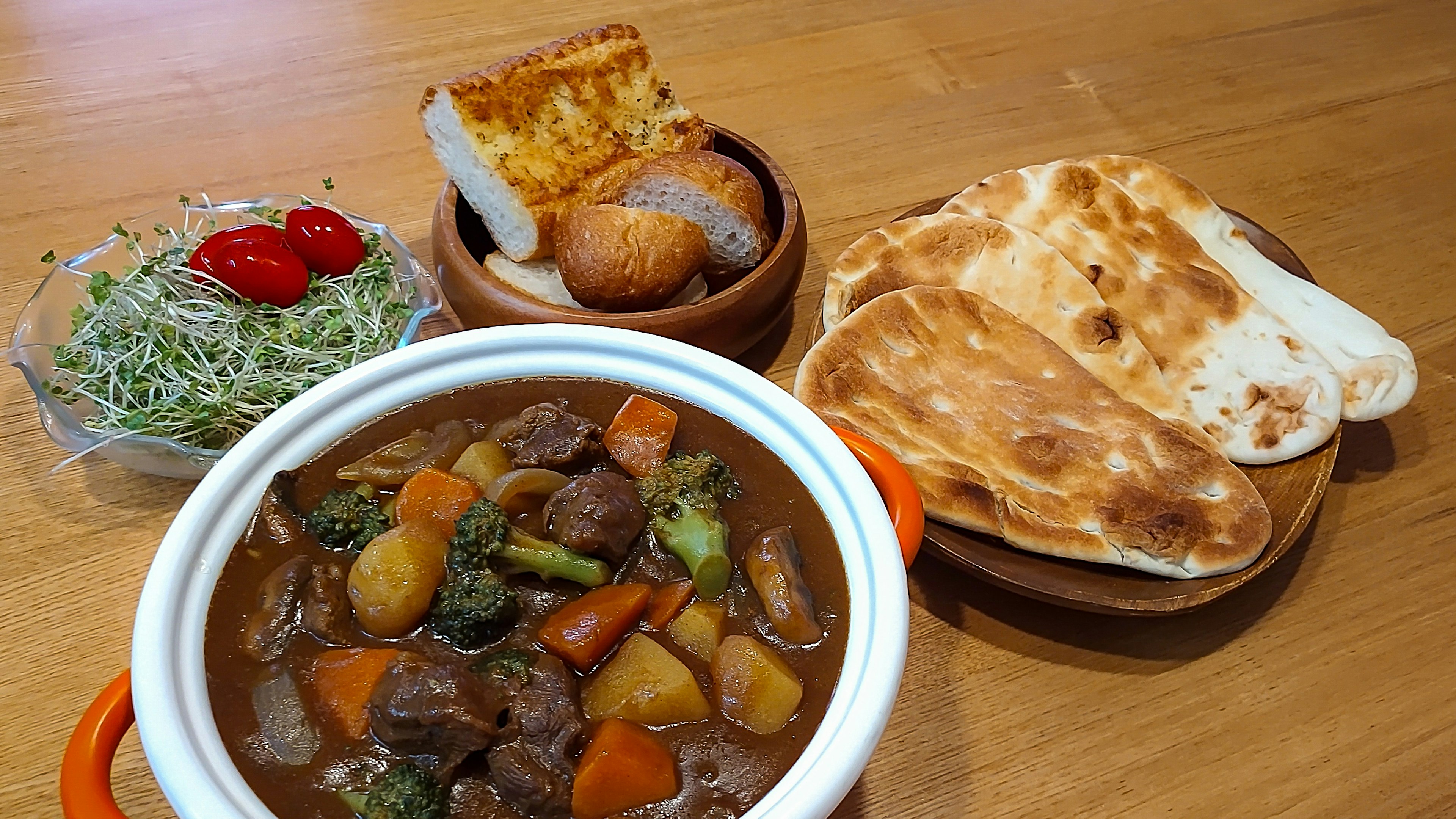 A delicious beef stew served with salad and assorted breads on a wooden table