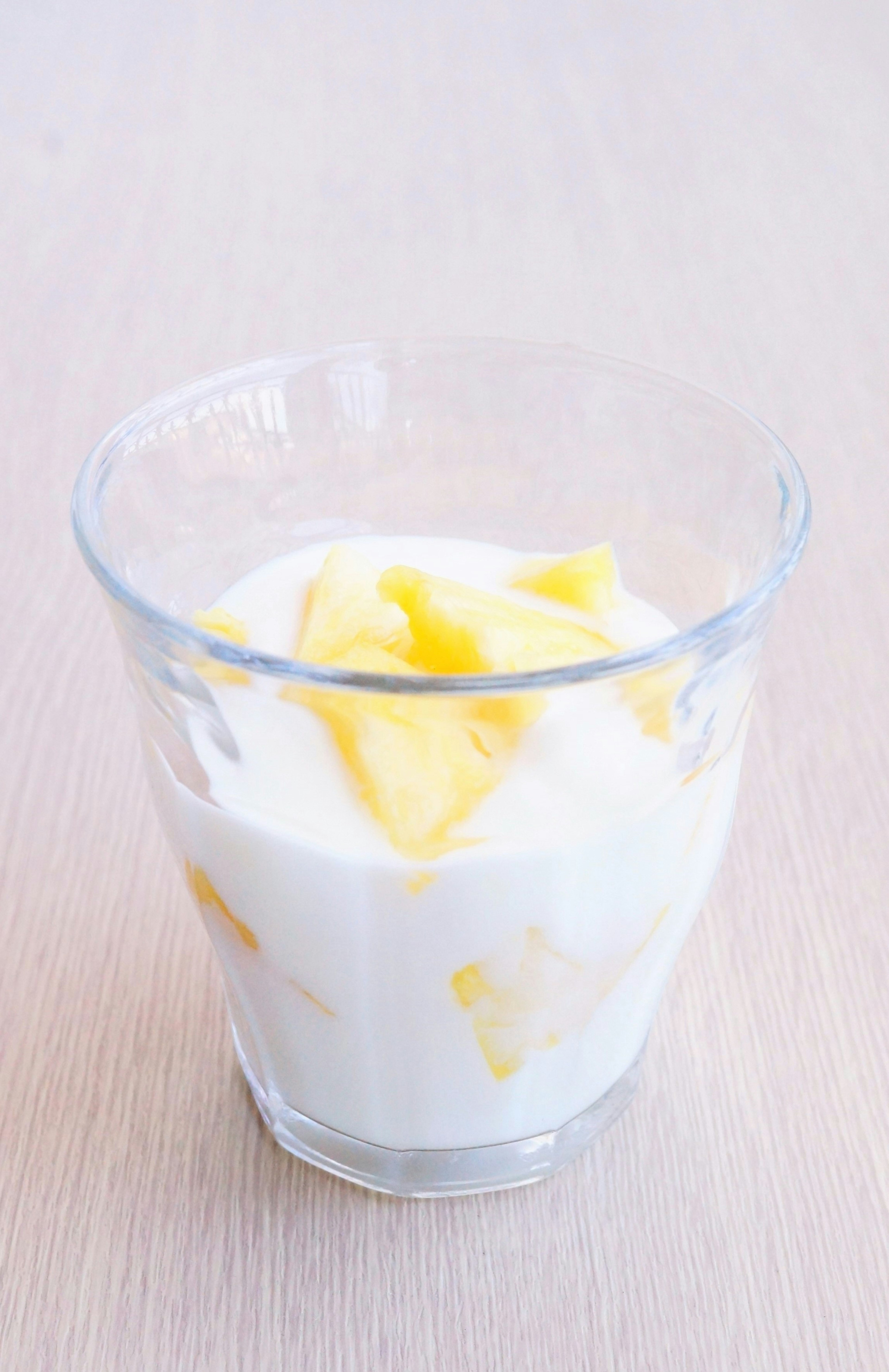 Secangkir kaca berisi yogurt dan irisan mangga