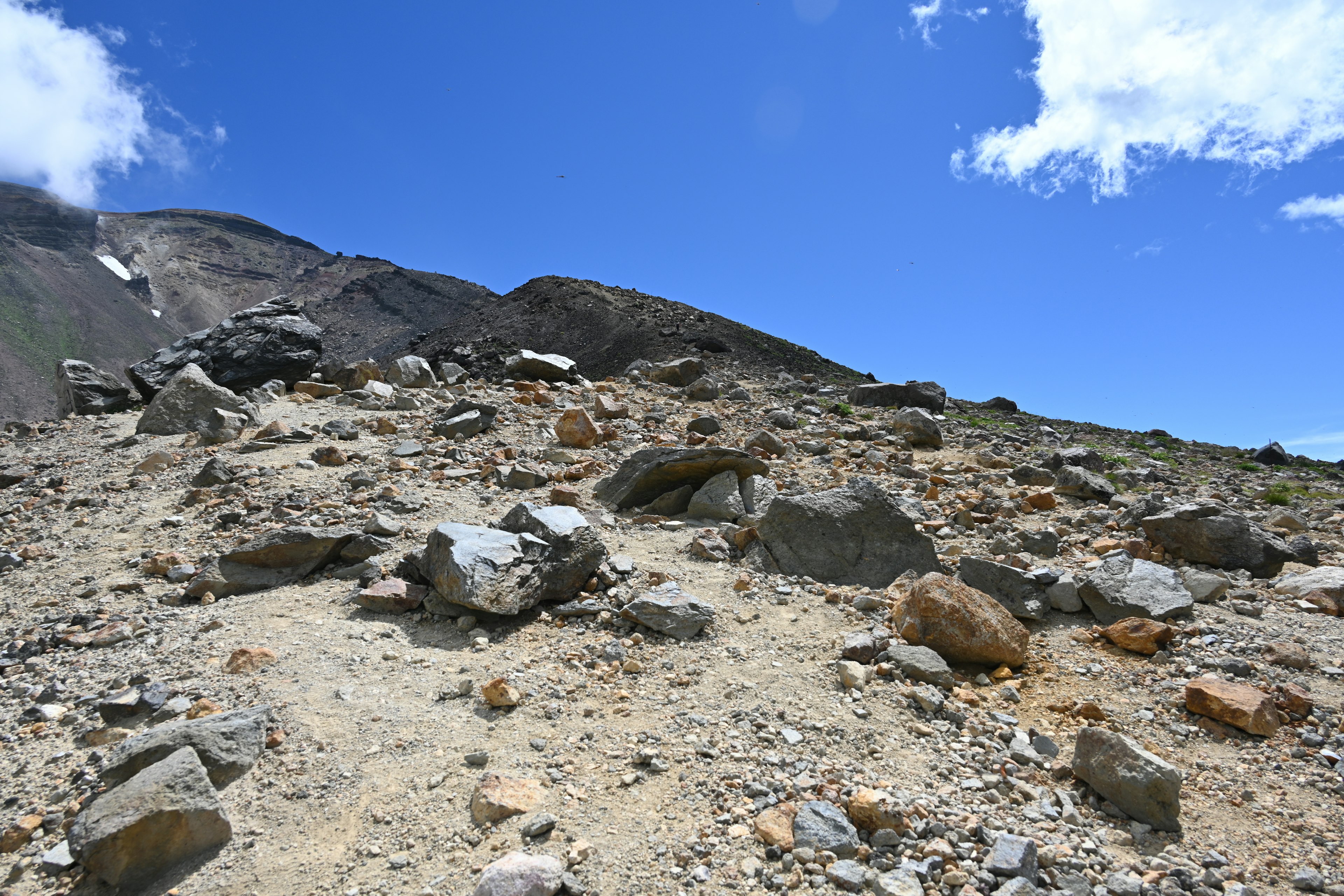 Pemandangan berbatu dan berpasir di lereng gunung dengan langit biru dan awan putih