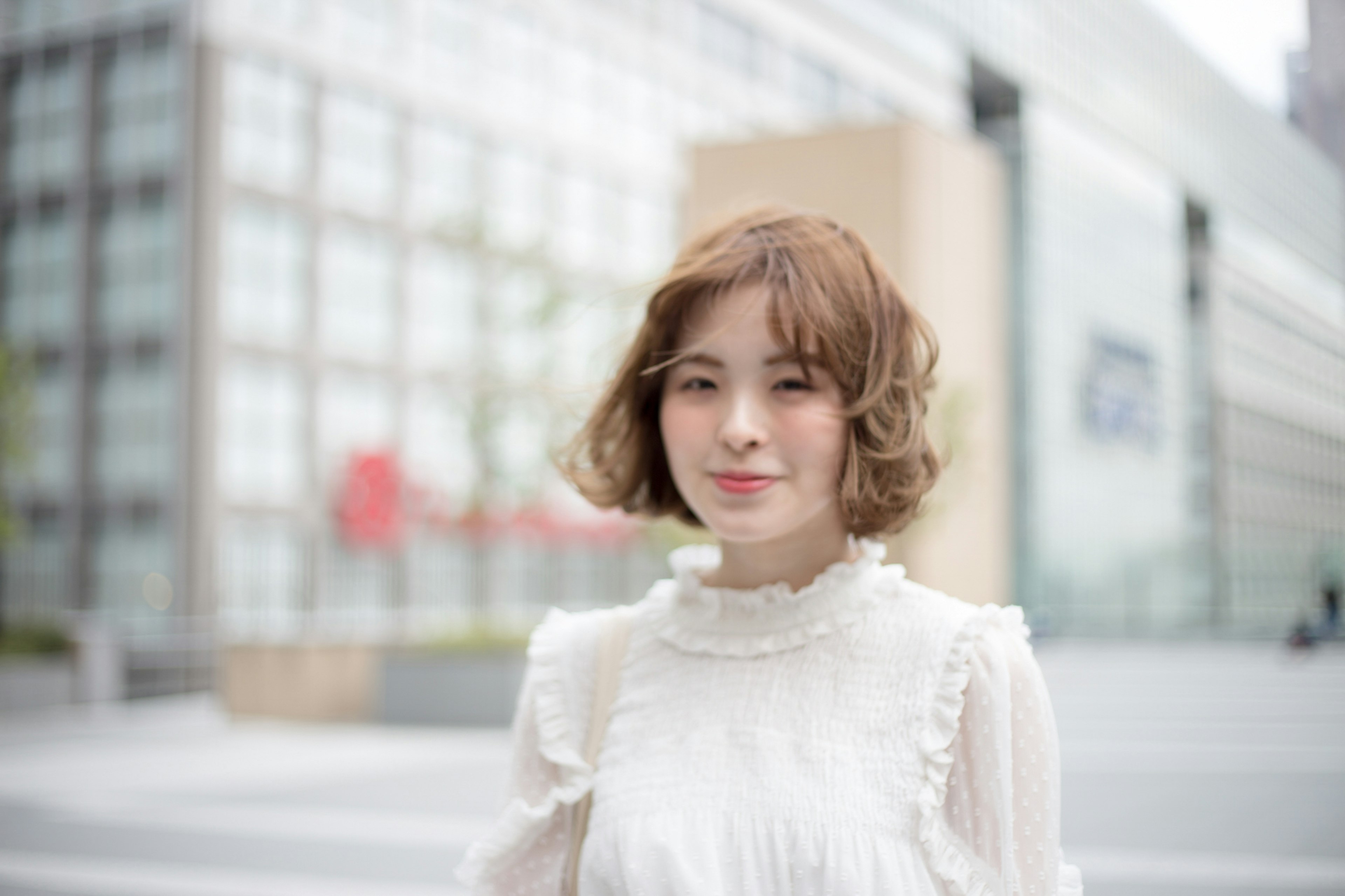 A young woman in a white blouse smiling on a city street with modern buildings in the background