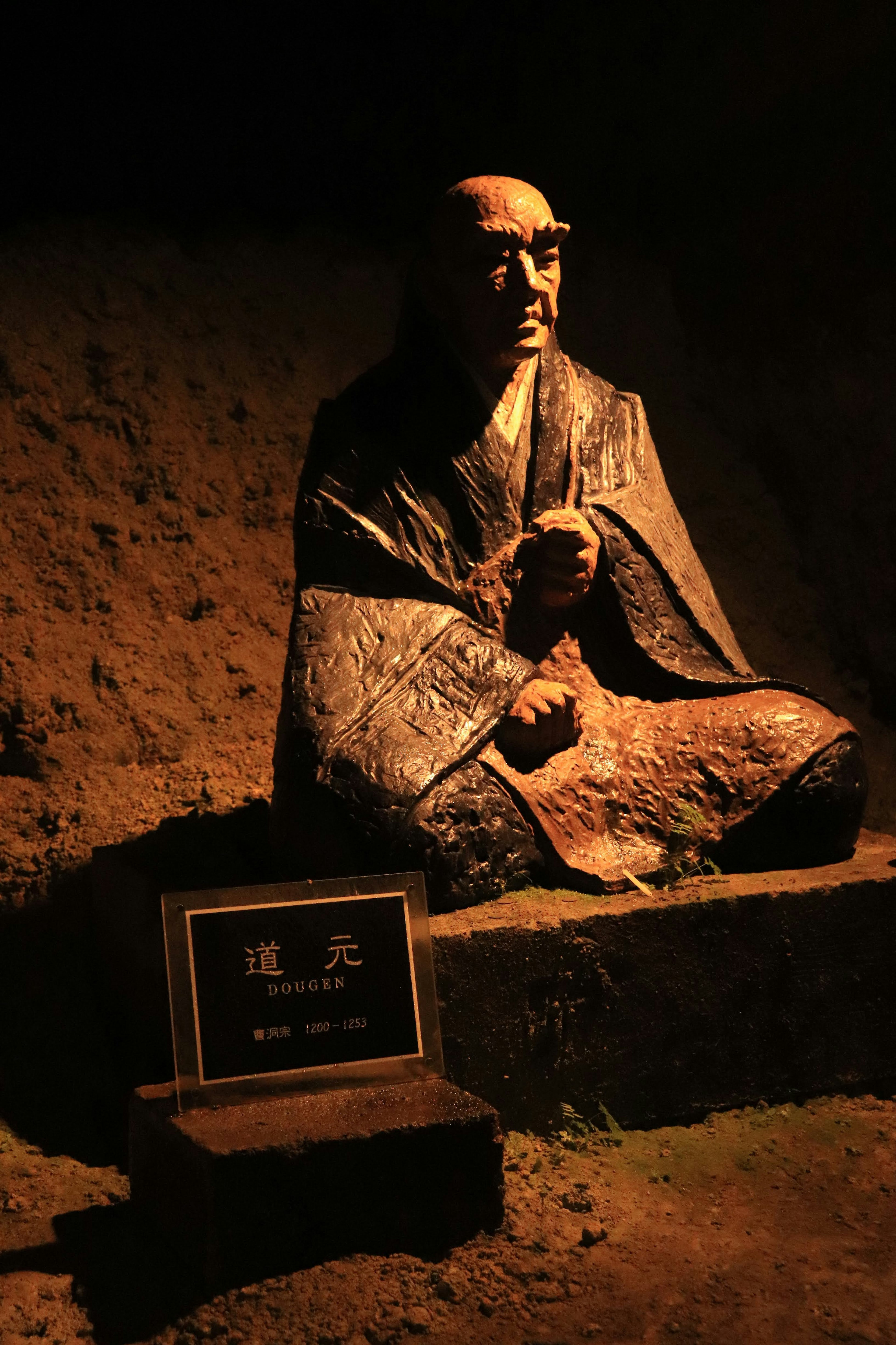 A seated statue of a monk in a dimly lit environment