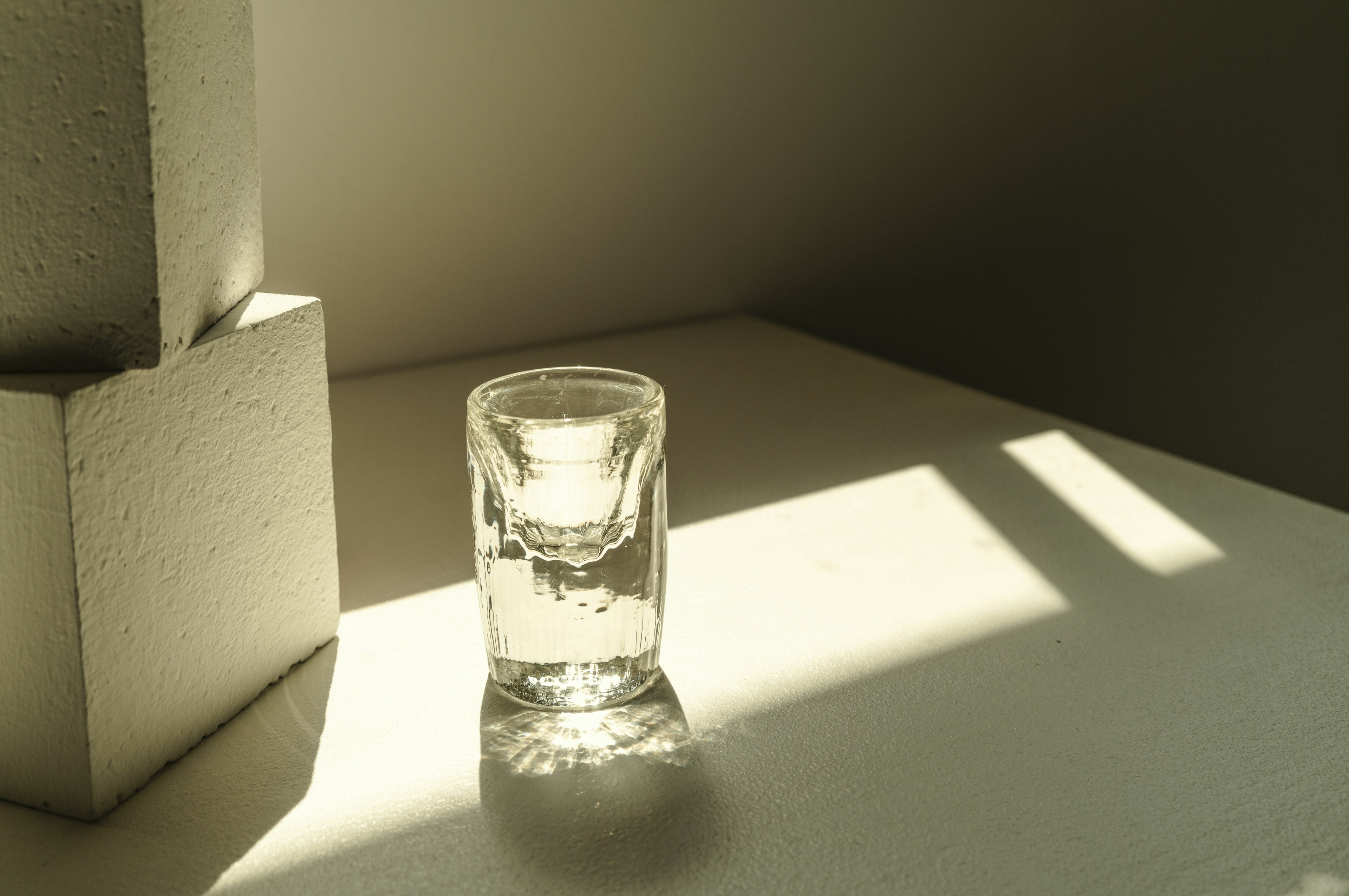 A clear shot glass illuminated by sunlight in a minimalist setting