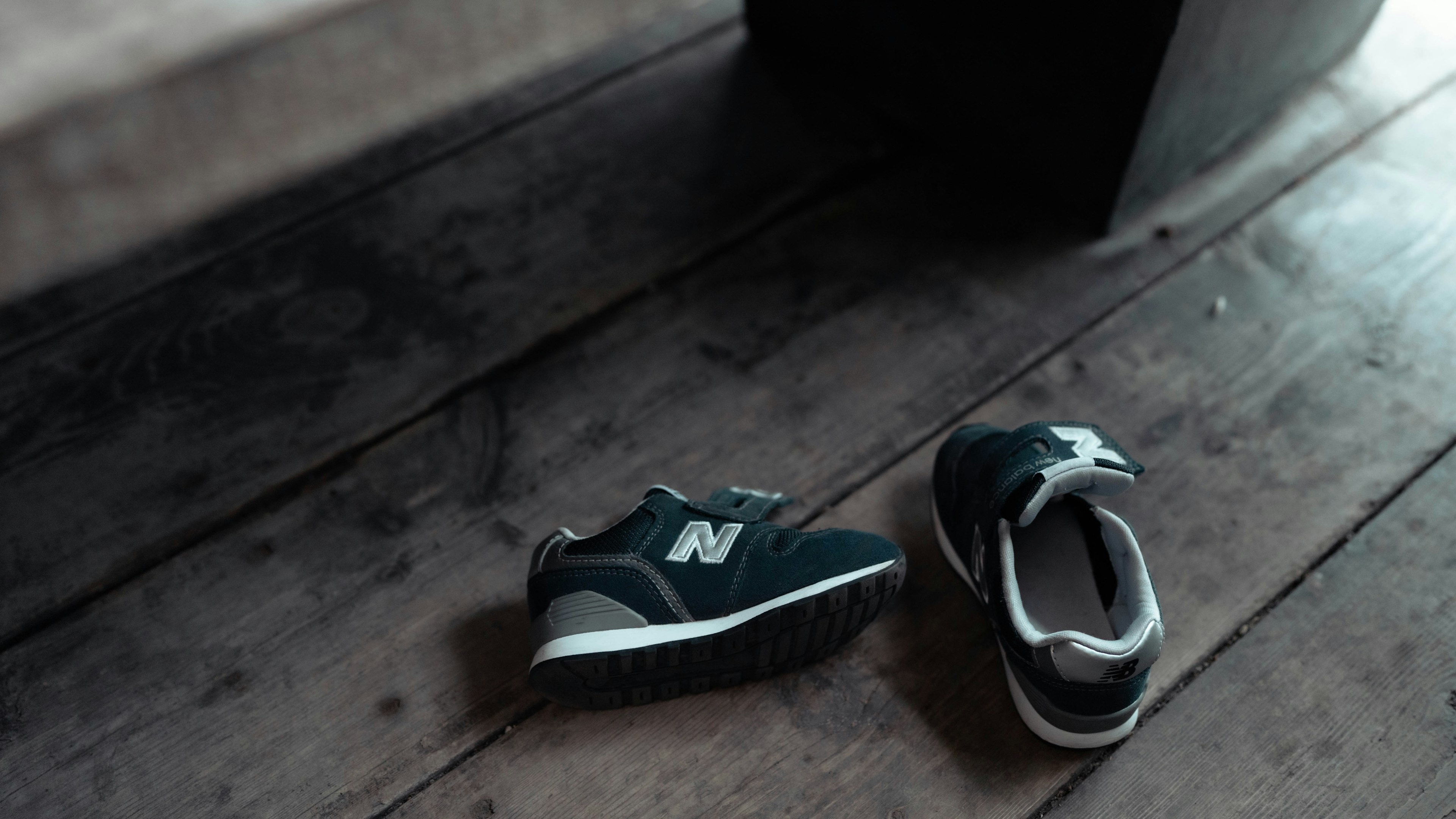 Two New Balance shoes placed on a wooden floor