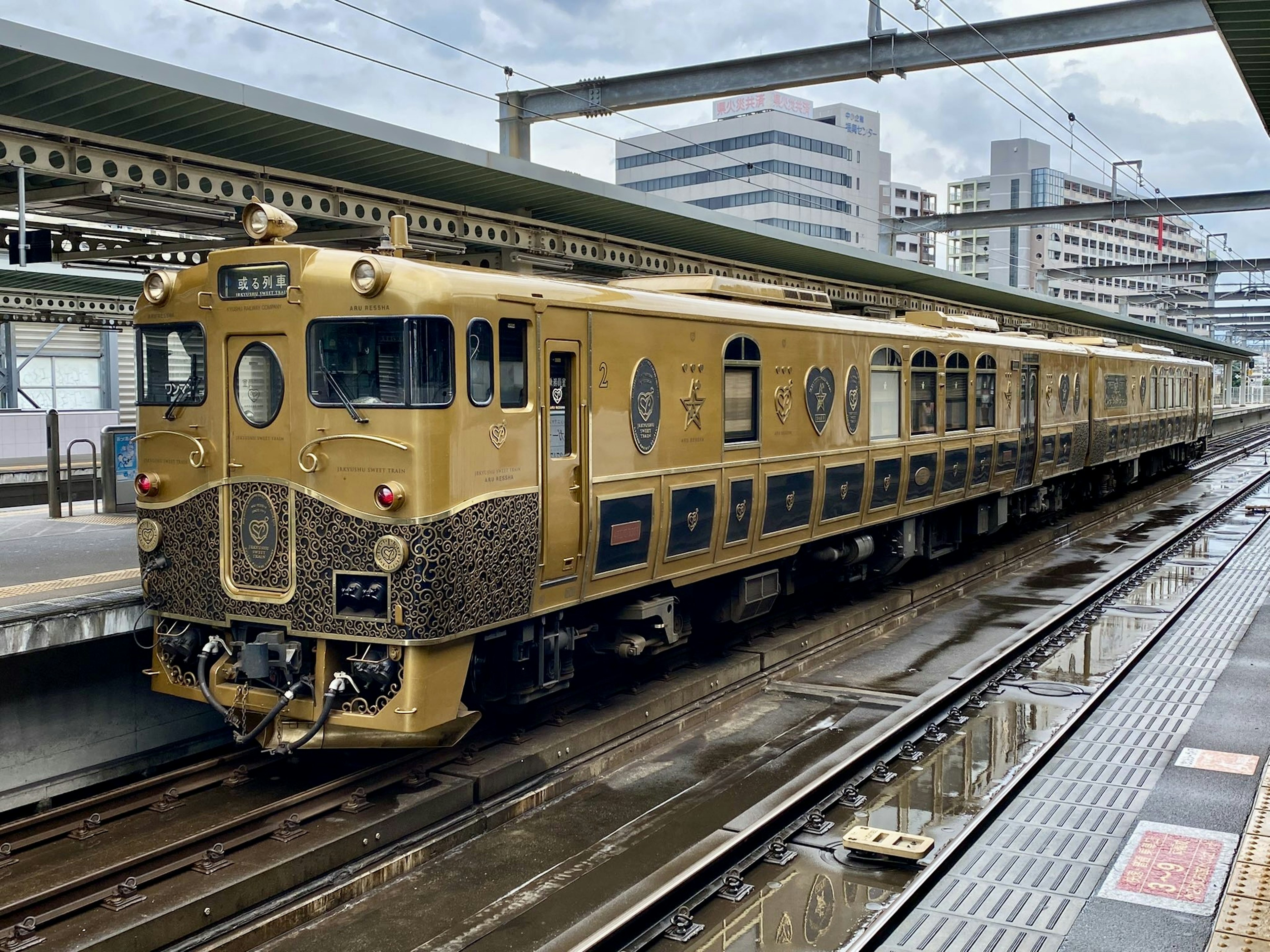 Golden train at a station with modern buildings in the background