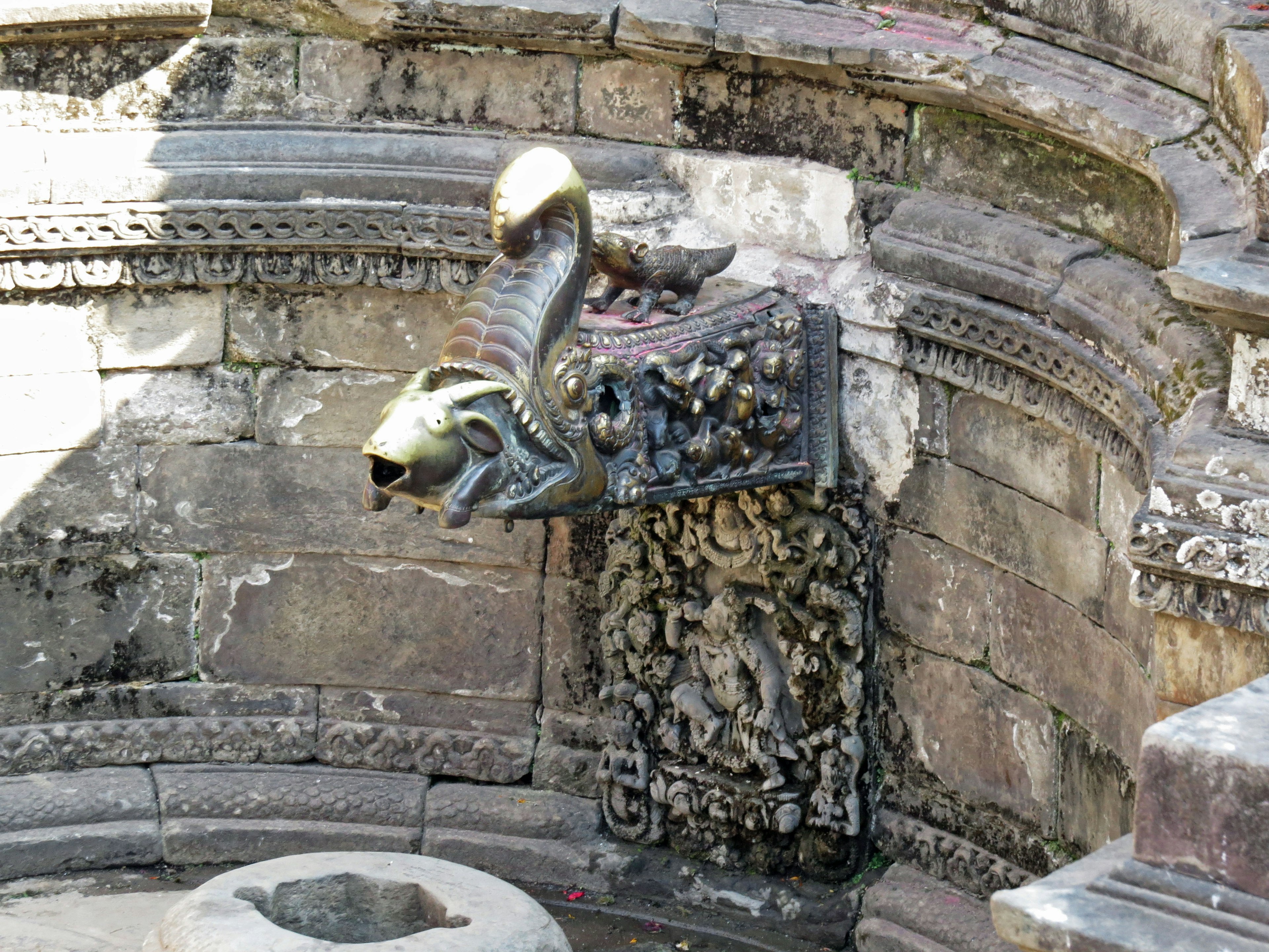 Partie d'une ancienne fontaine avec des sculptures décoratives et une tête de serpent distinctive