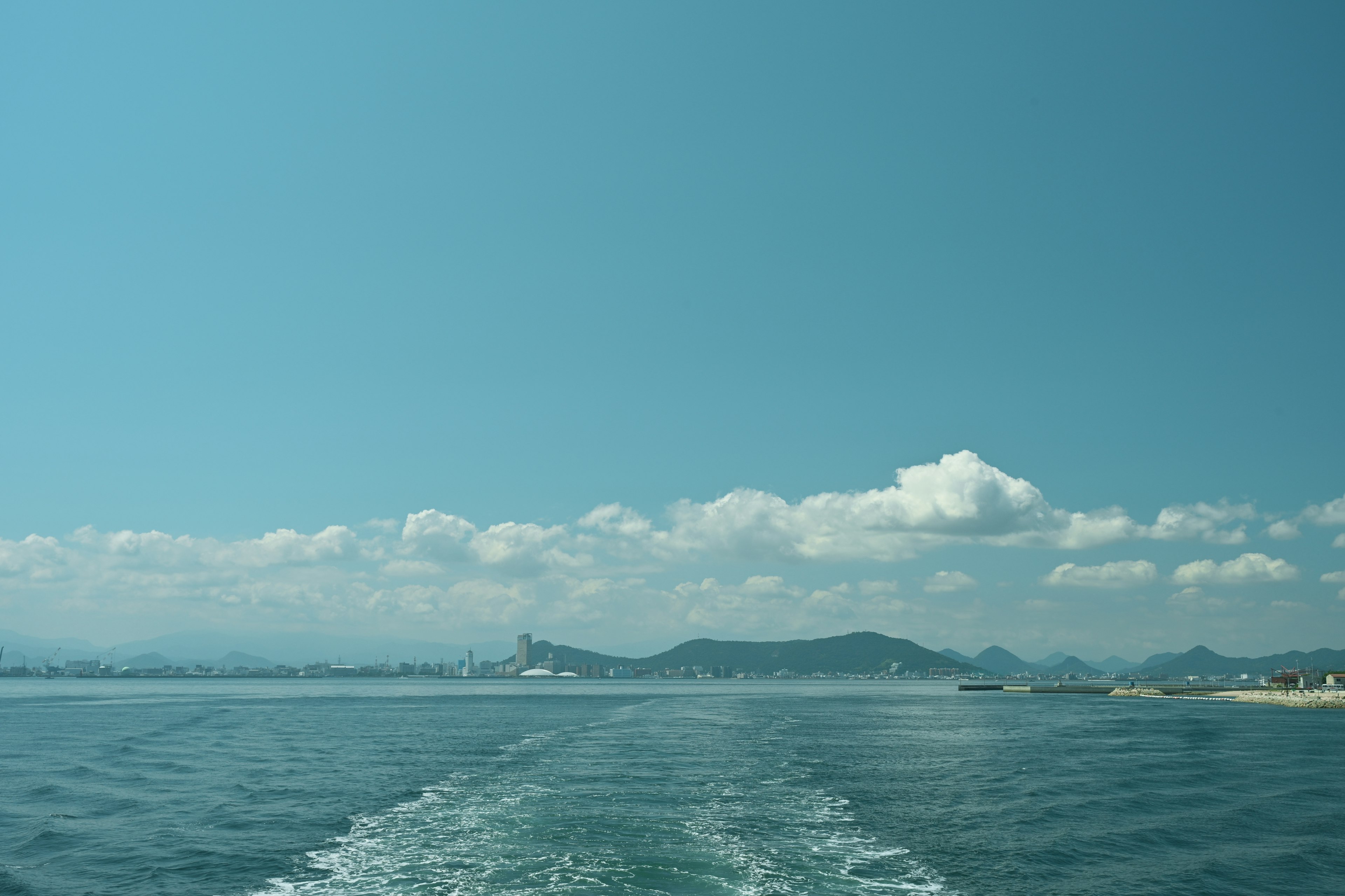 Blue ocean with clouds in the sky boat wake visible on the water