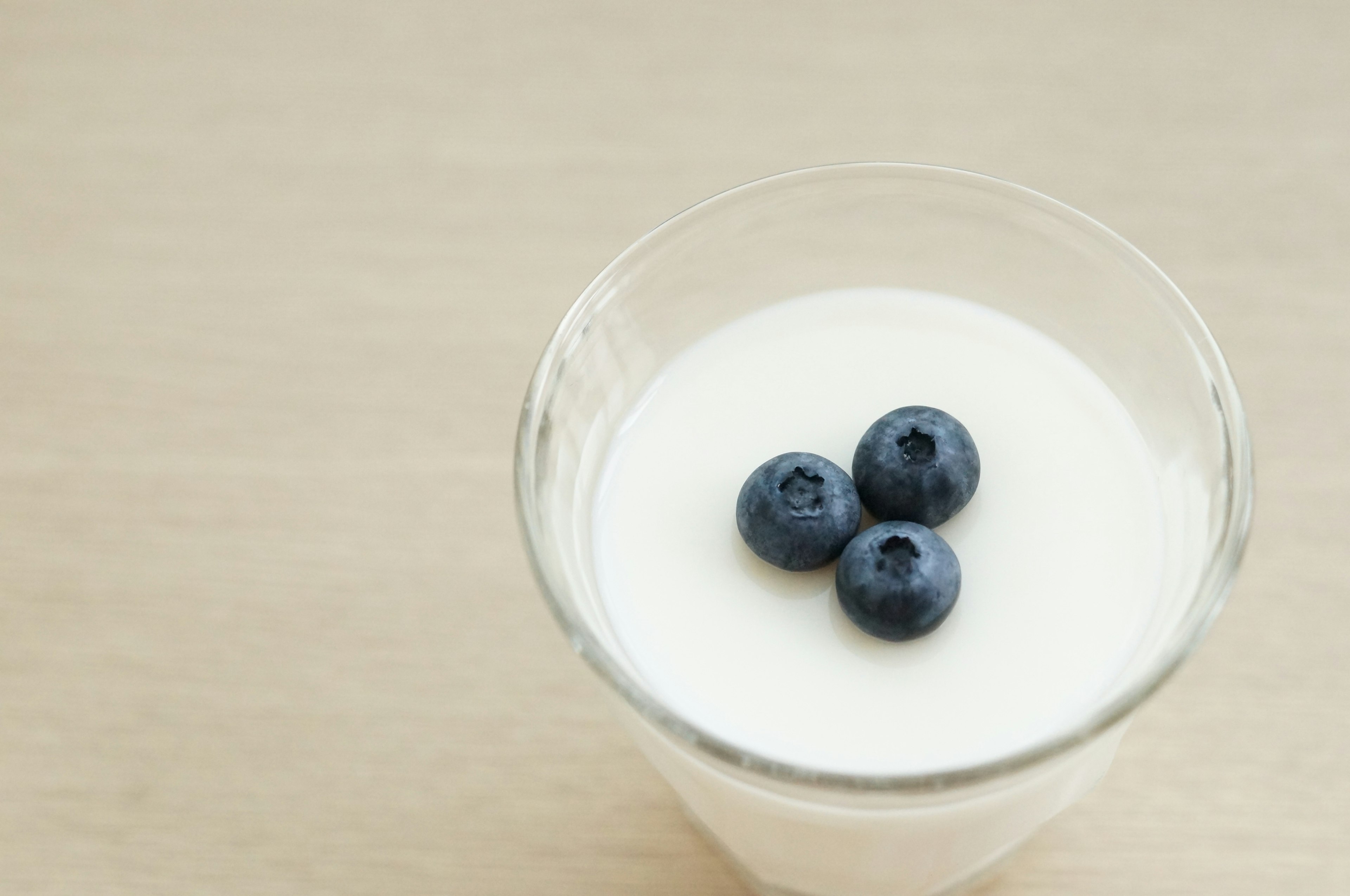 A glass bowl of yogurt topped with three blueberries