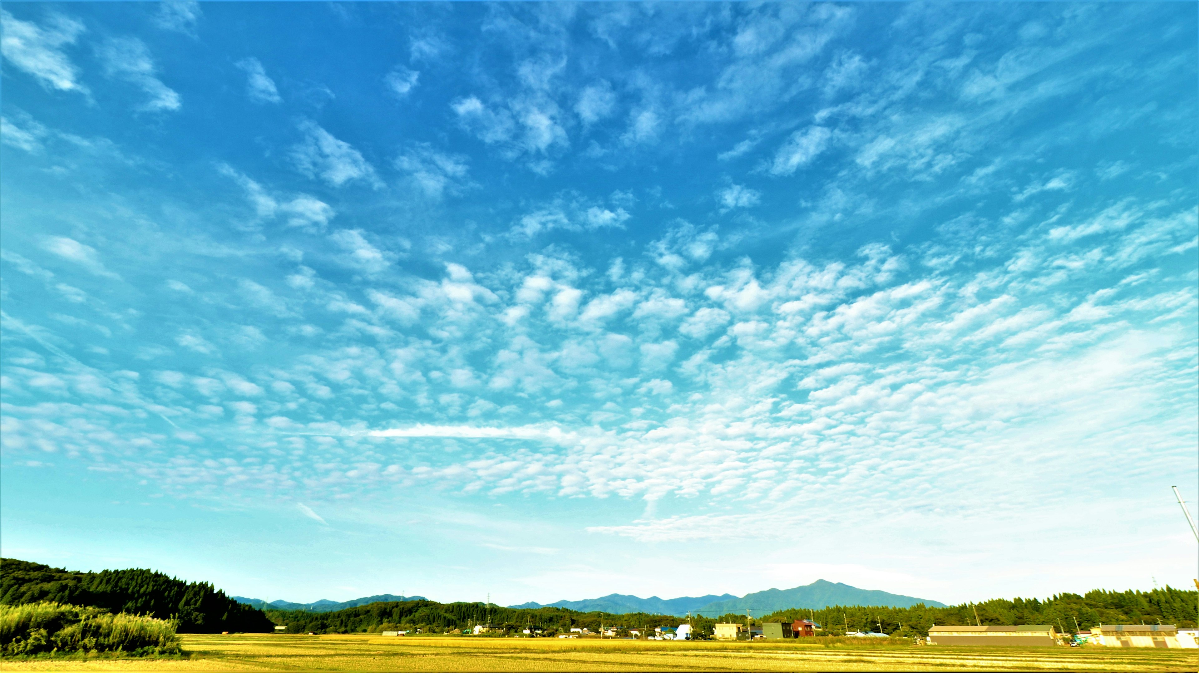 Amplio cielo azul con nubes montañas y campos al fondo