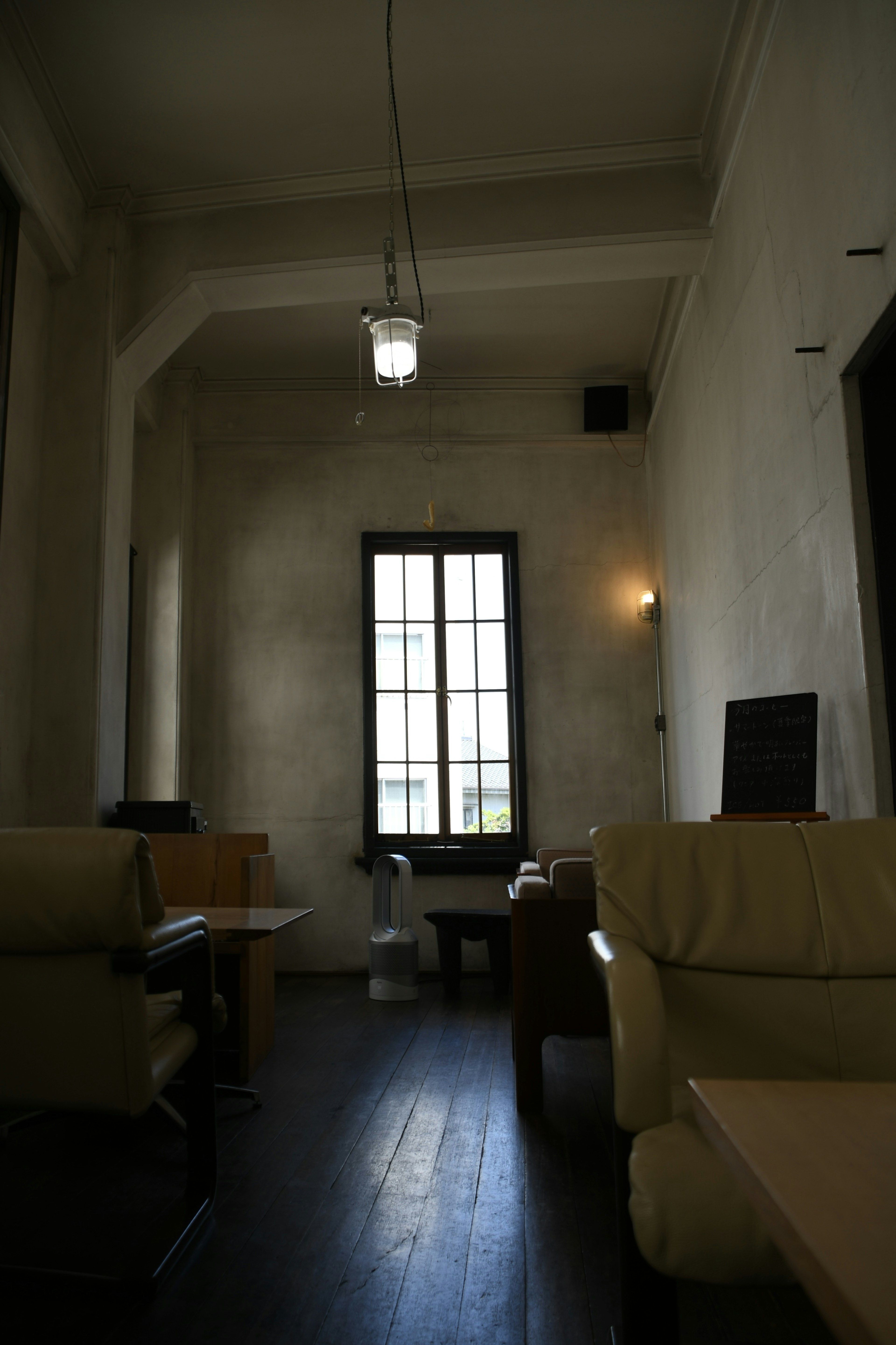 A simple room with white walls and a black floor featuring a large window and sofas