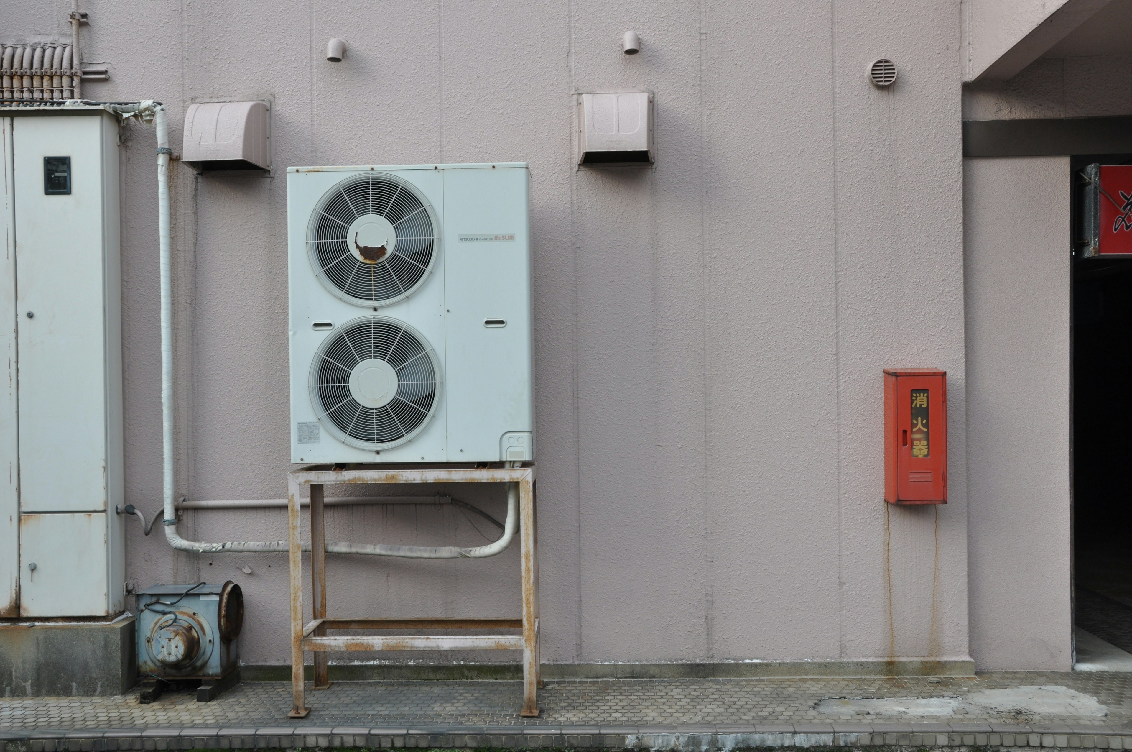 Air conditioning unit mounted on a wall next to a red telephone box