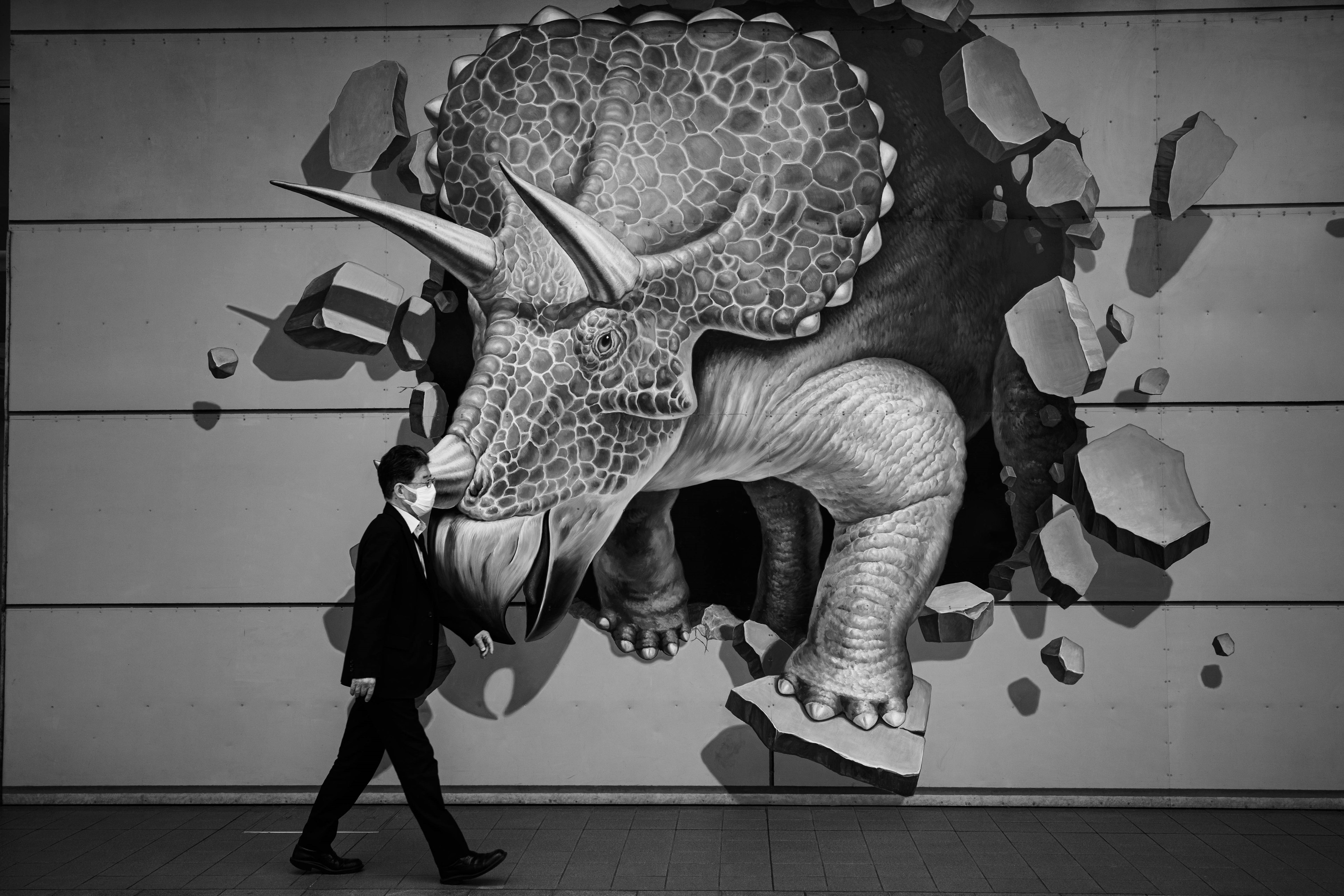 A 3D mural of a triceratops breaking through a wall with a suited man walking by