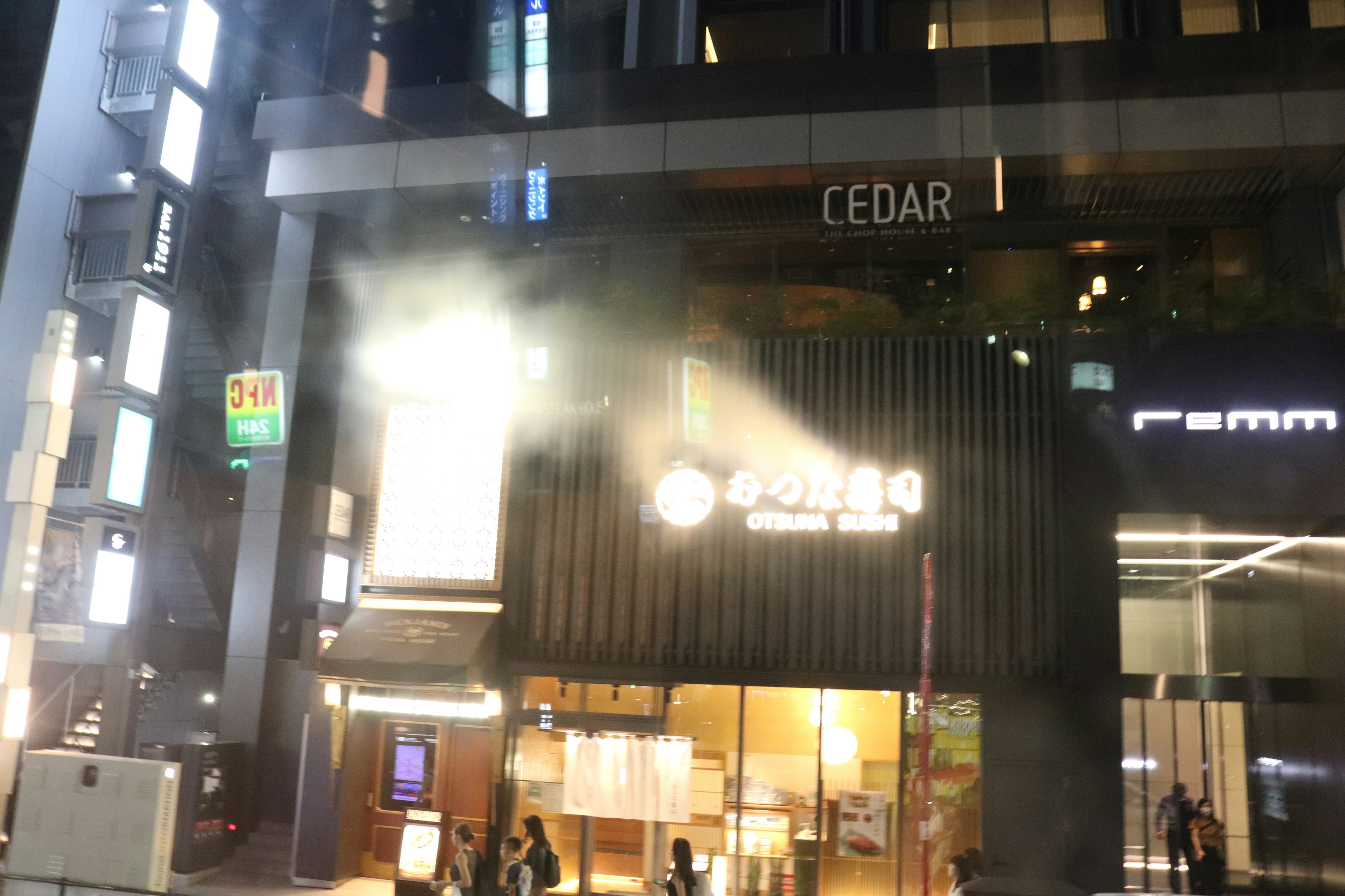 夜の街並みで明かりが灯るCEDARの外観と煙