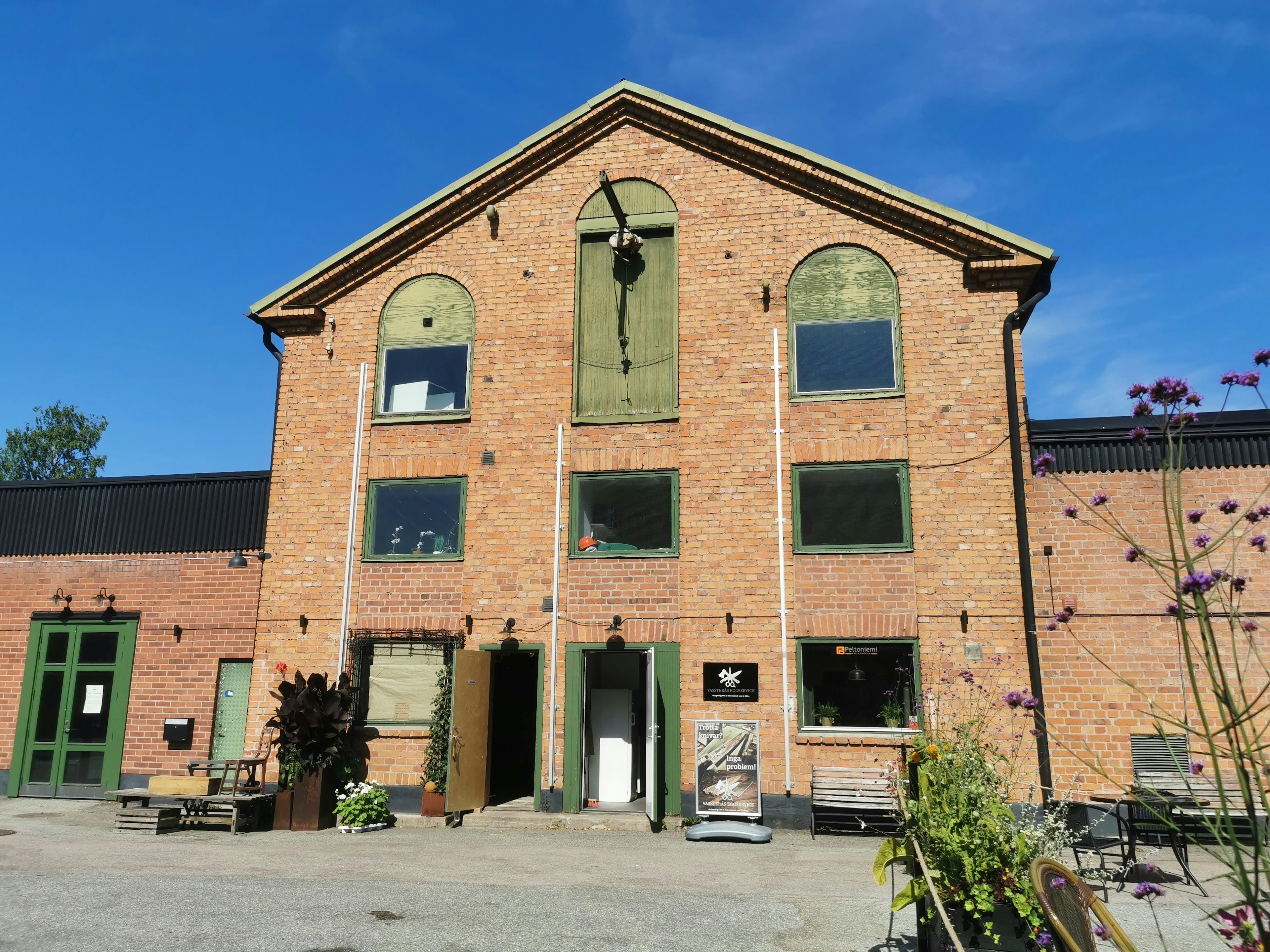 Exterior view of a red brick building with green windows and doors under a blue sky