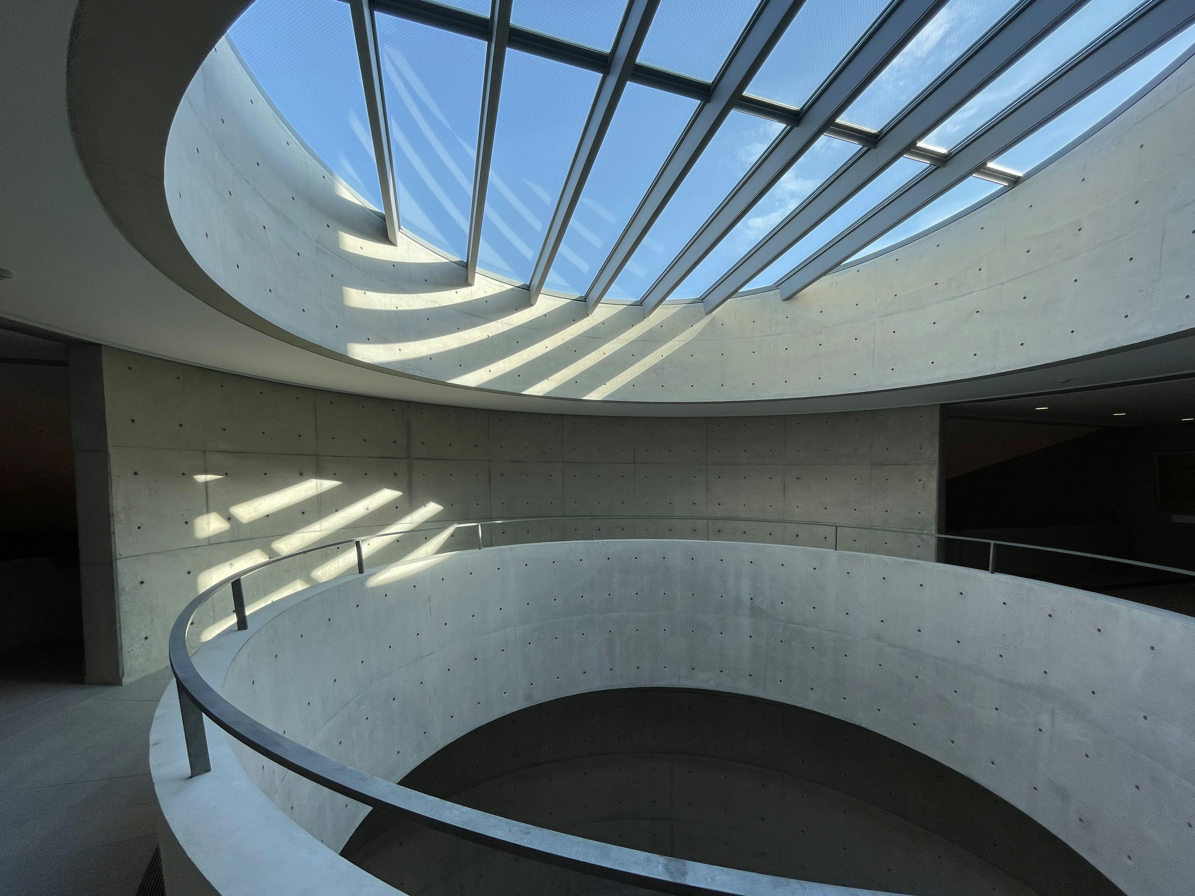 Interior of a building featuring a circular staircase and concrete walls Skylight casting shadows on the surface