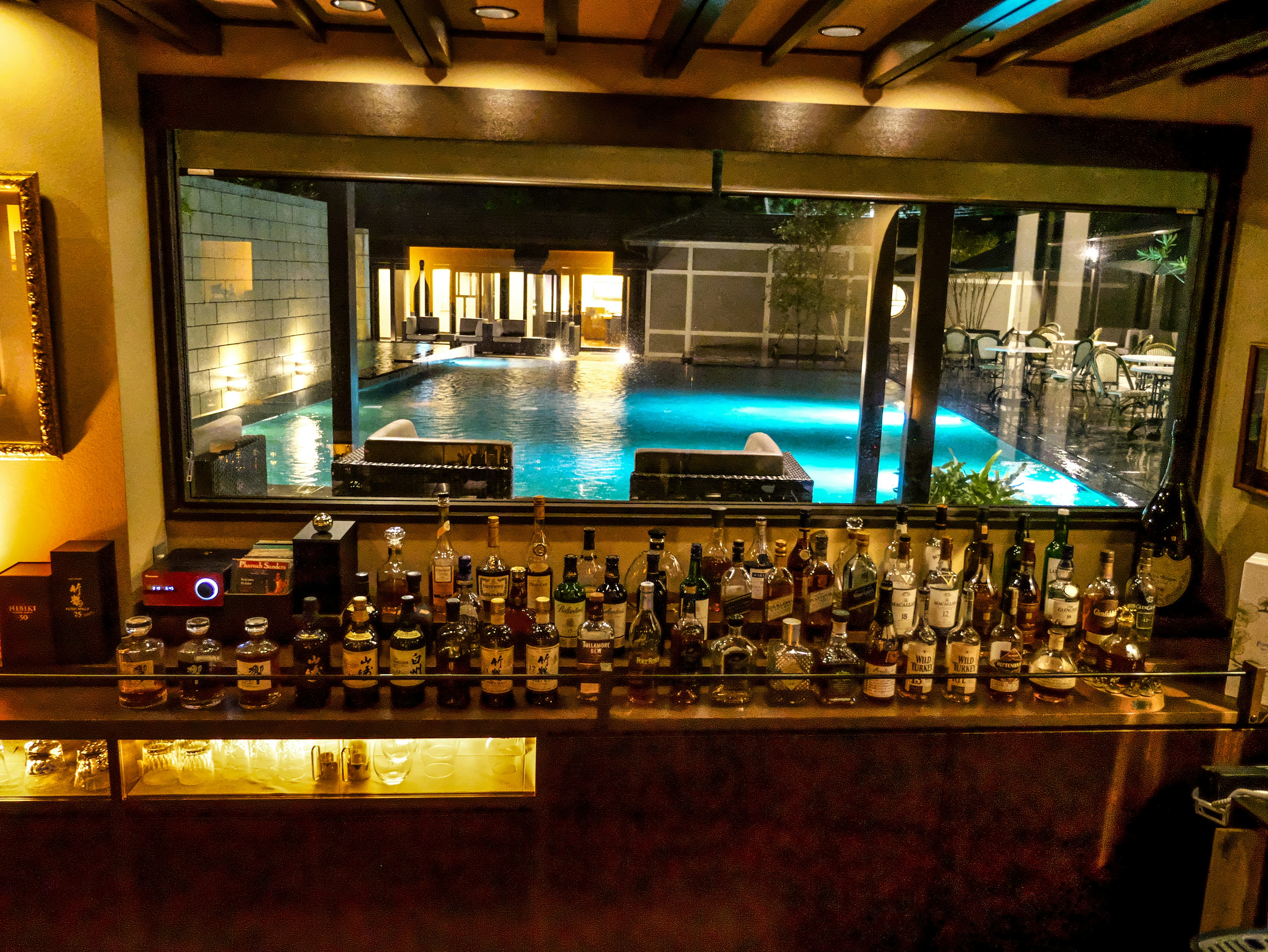 View of a stylish bar counter overlooking a lit pool and lounge area at night