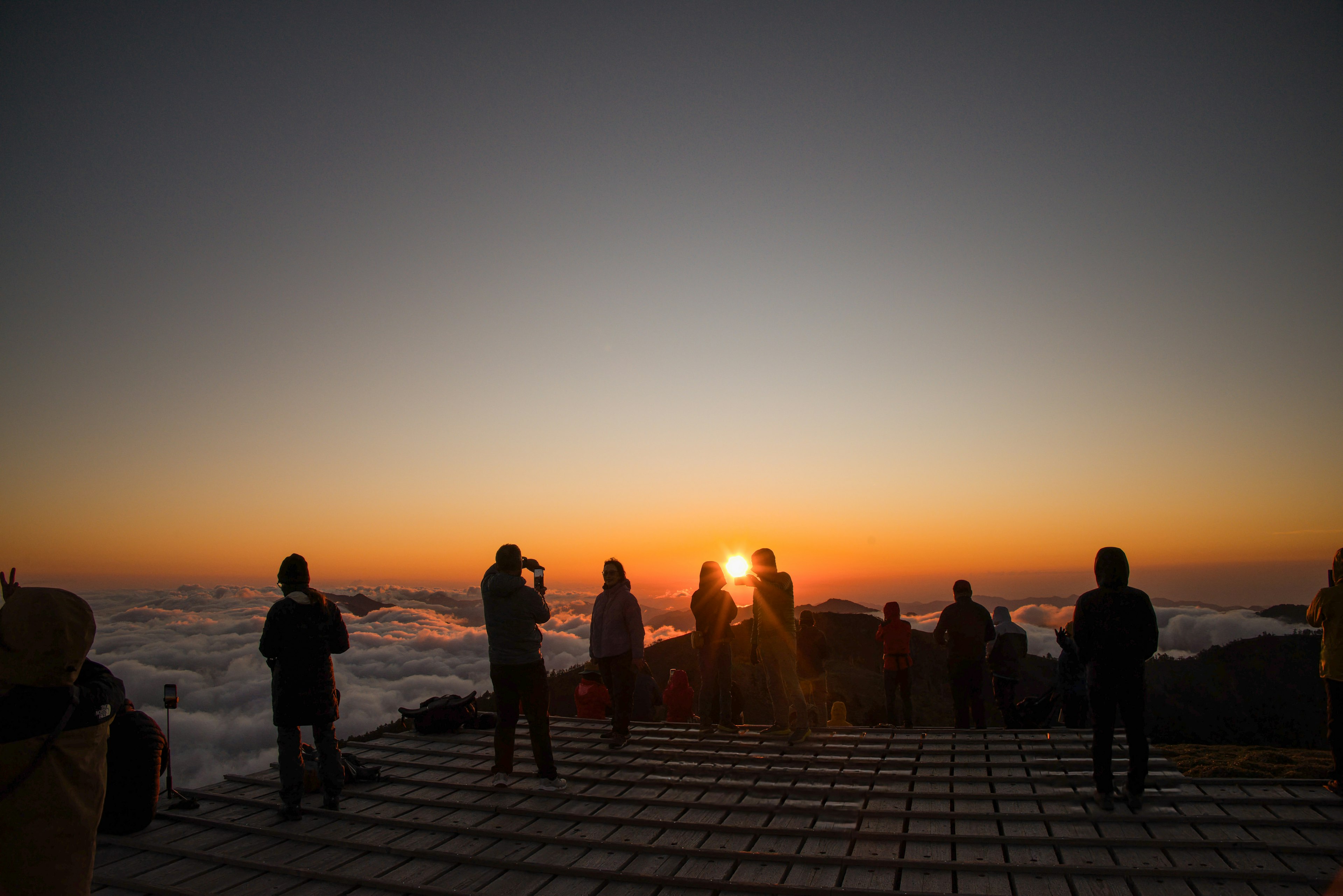 Personnes en silhouette se rassemblant au sommet d'une montagne avec un coucher de soleil en arrière-plan