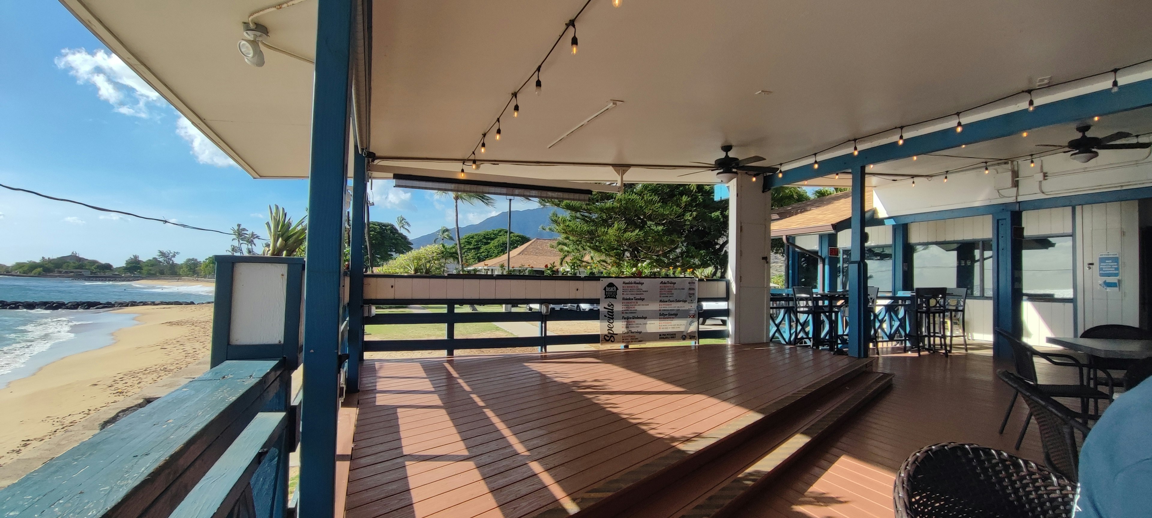 Terrace of a beachfront cafe featuring blue pillars and wooden flooring