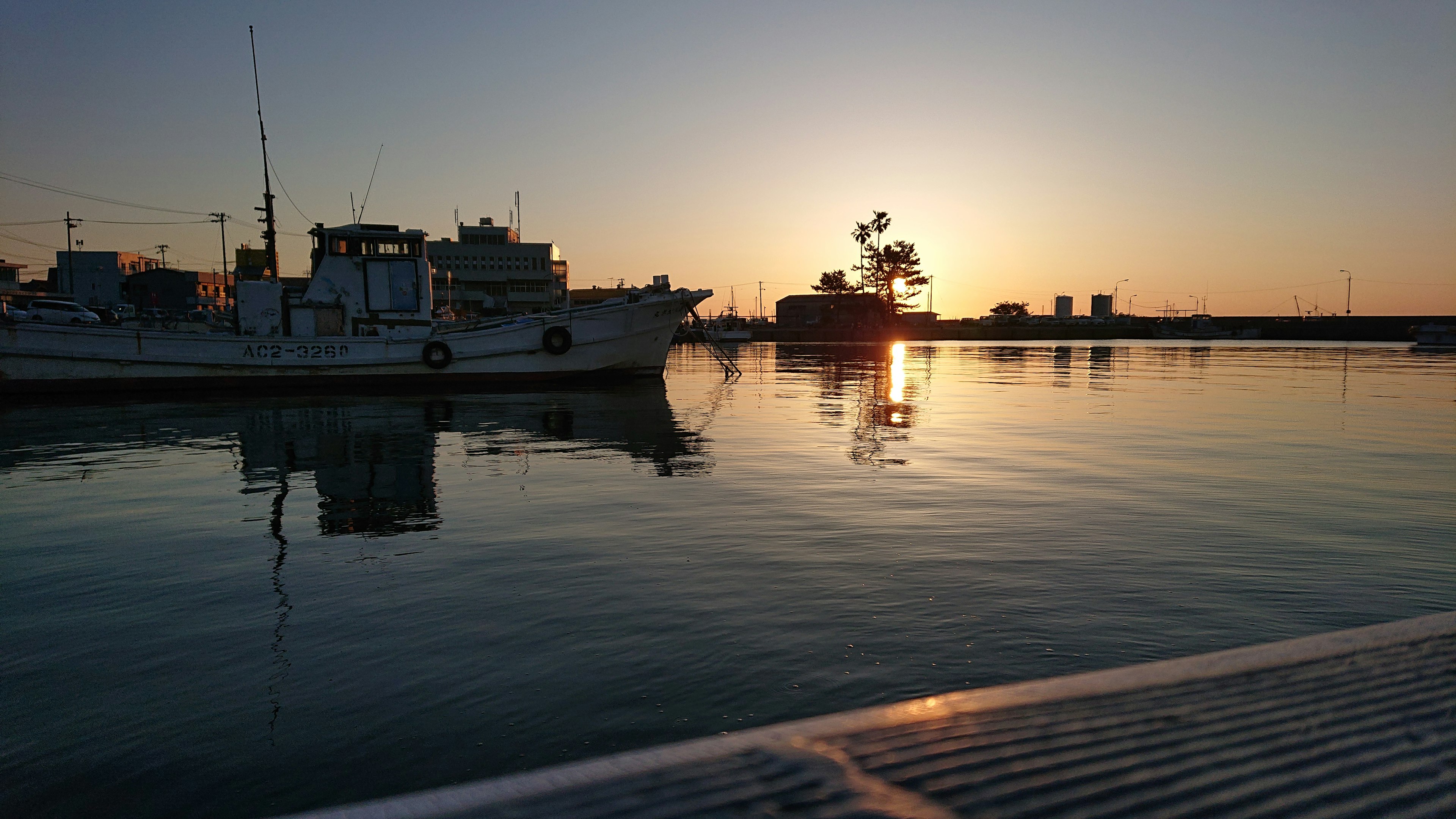 Scène de port paisible avec des bateaux silhouettés contre un coucher de soleil et des eaux calmes