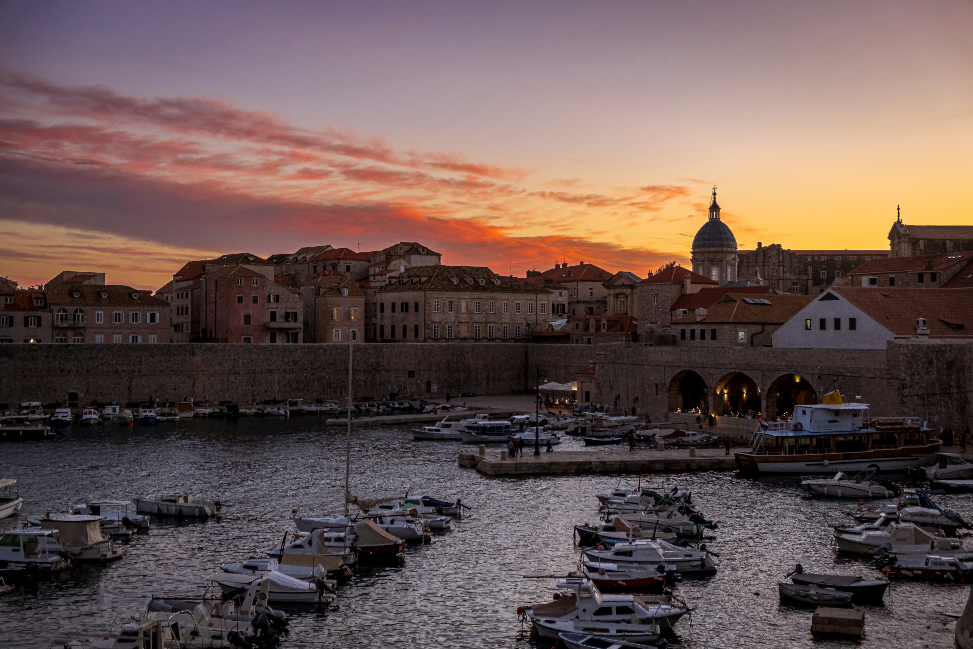 Pelabuhan Dubrovnik saat matahari terbenam dengan perahu dan bangunan bersejarah