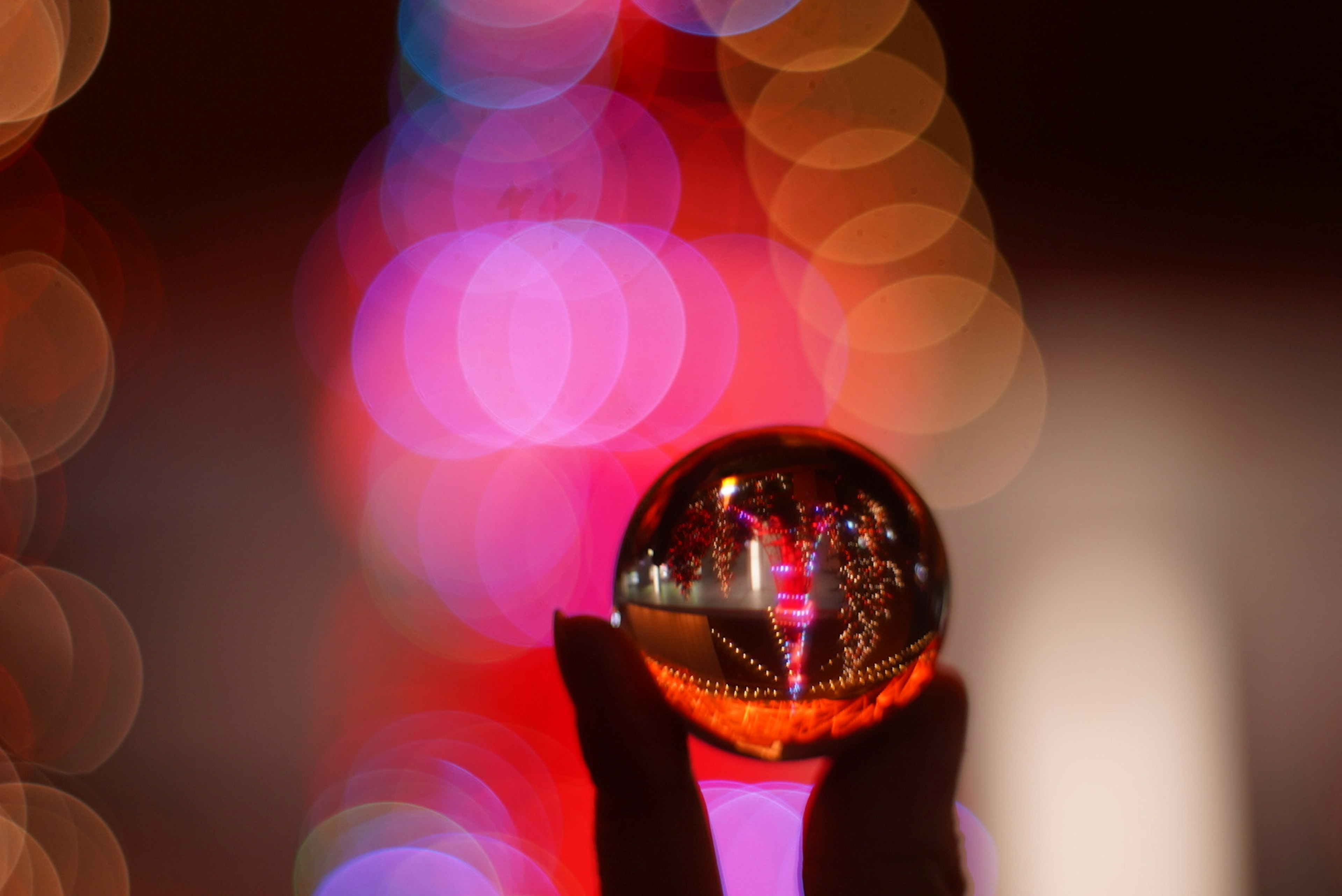 Una sfera di cristallo trasparente tenuta in mano che riflette un bokeh vibrante sullo sfondo