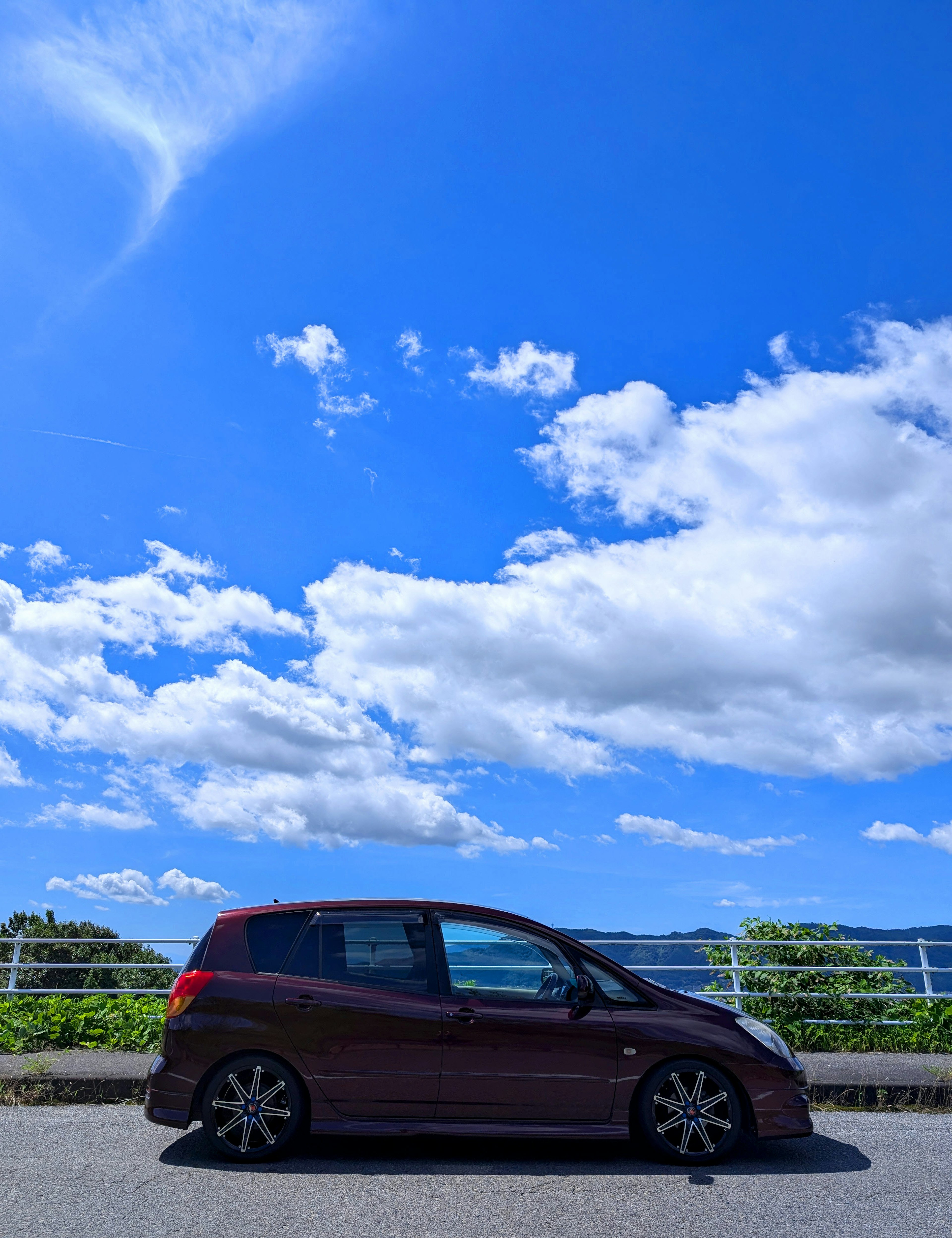 Red car parked under a blue sky with white clouds