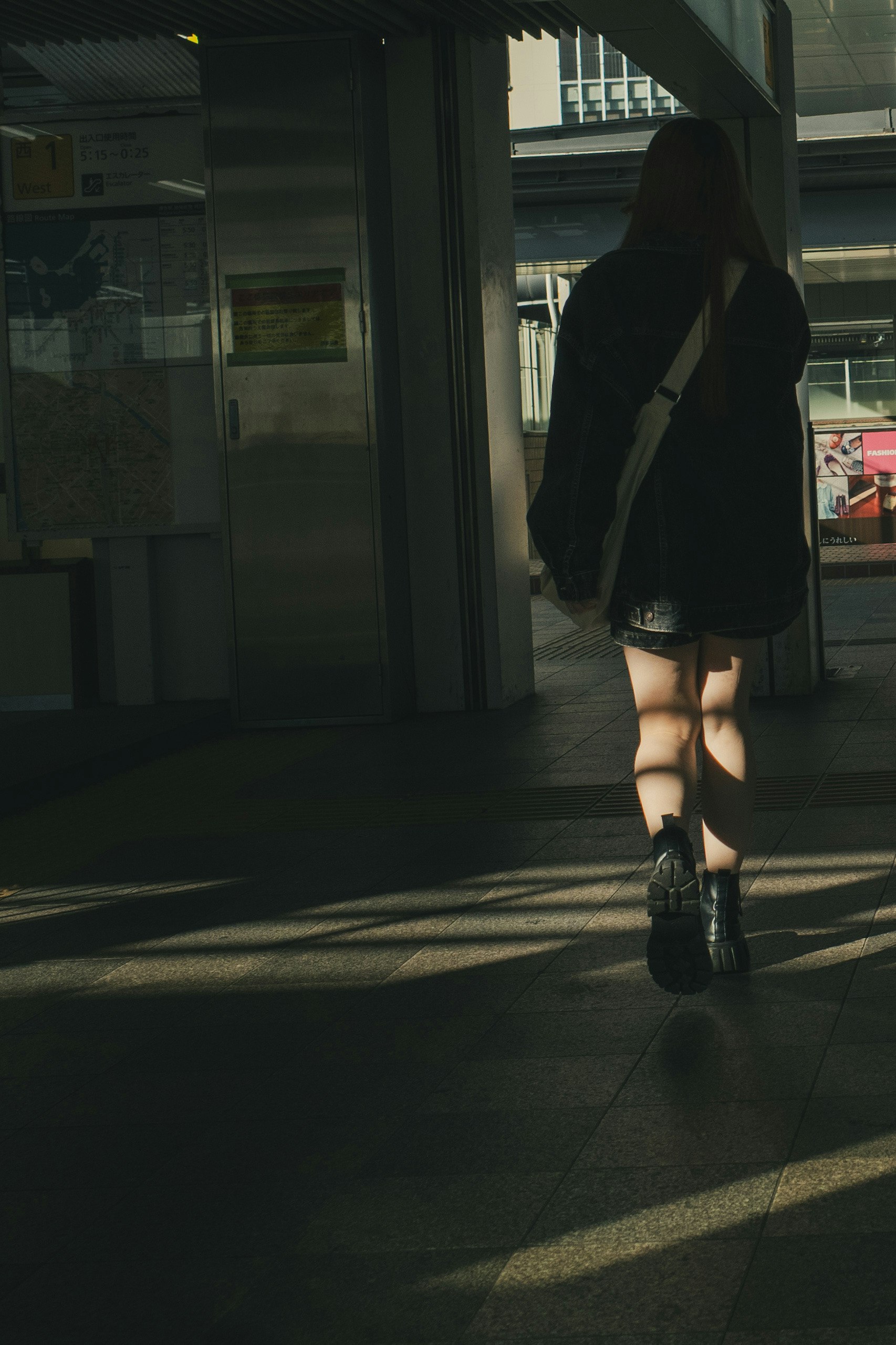 Una donna che cammina in un corridoio poco illuminato indossando abiti neri e stivali con contrasto di luce e ombra