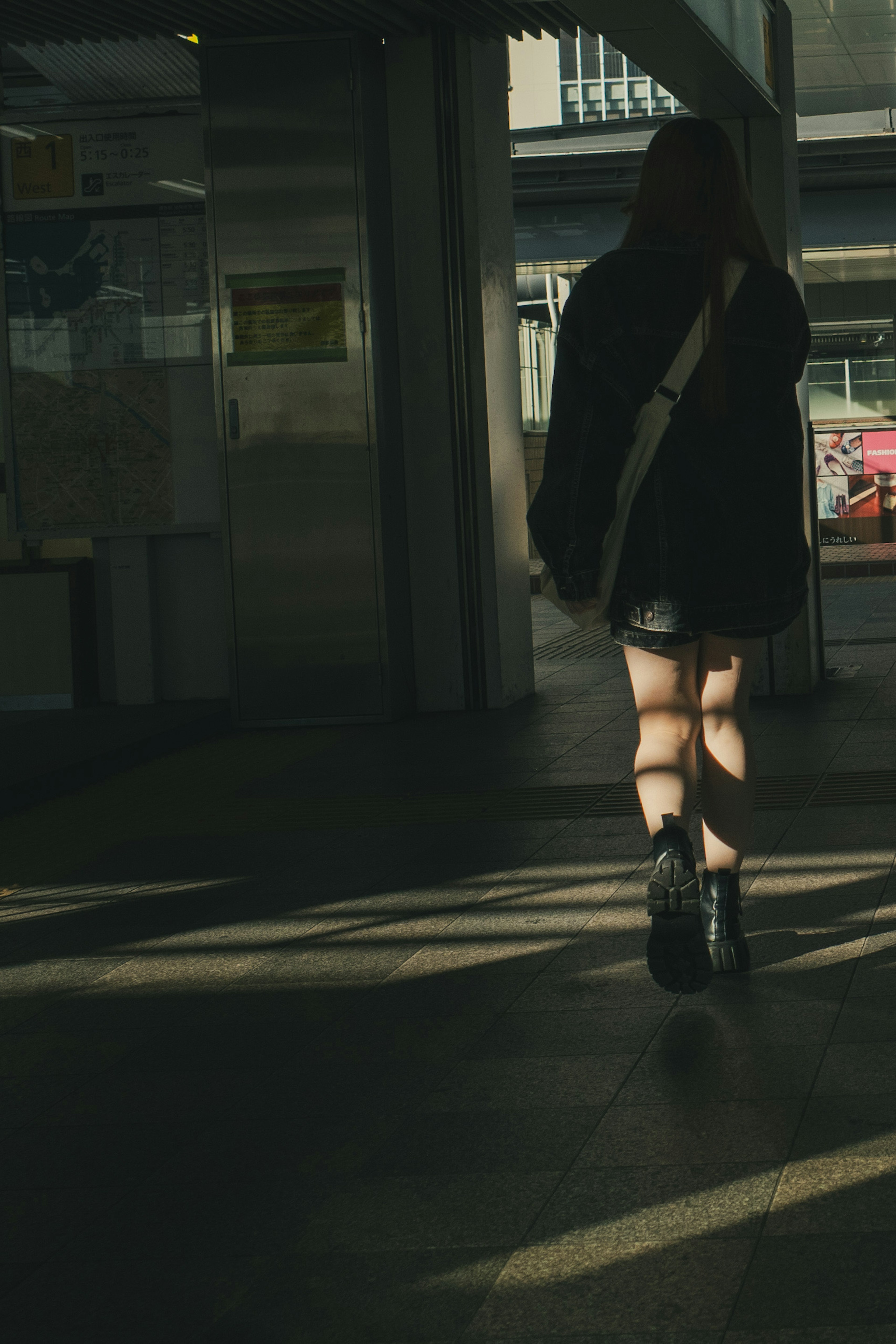 Una mujer caminando en un pasillo poco iluminado vestida con ropa negra y botas con contraste de luz y sombra