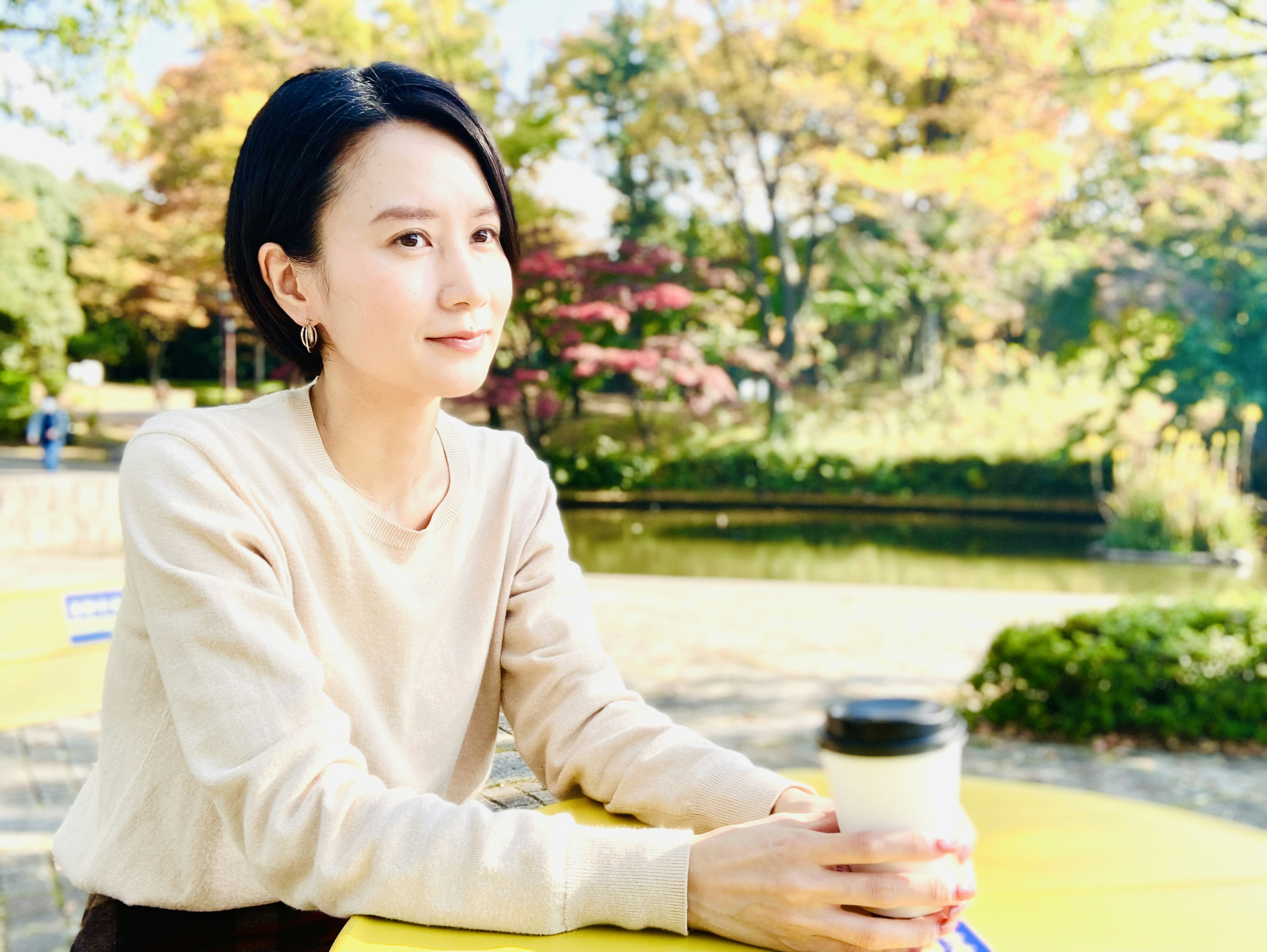 Retrato de una mujer sosteniendo un café en un parque con un hermoso fondo otoñal