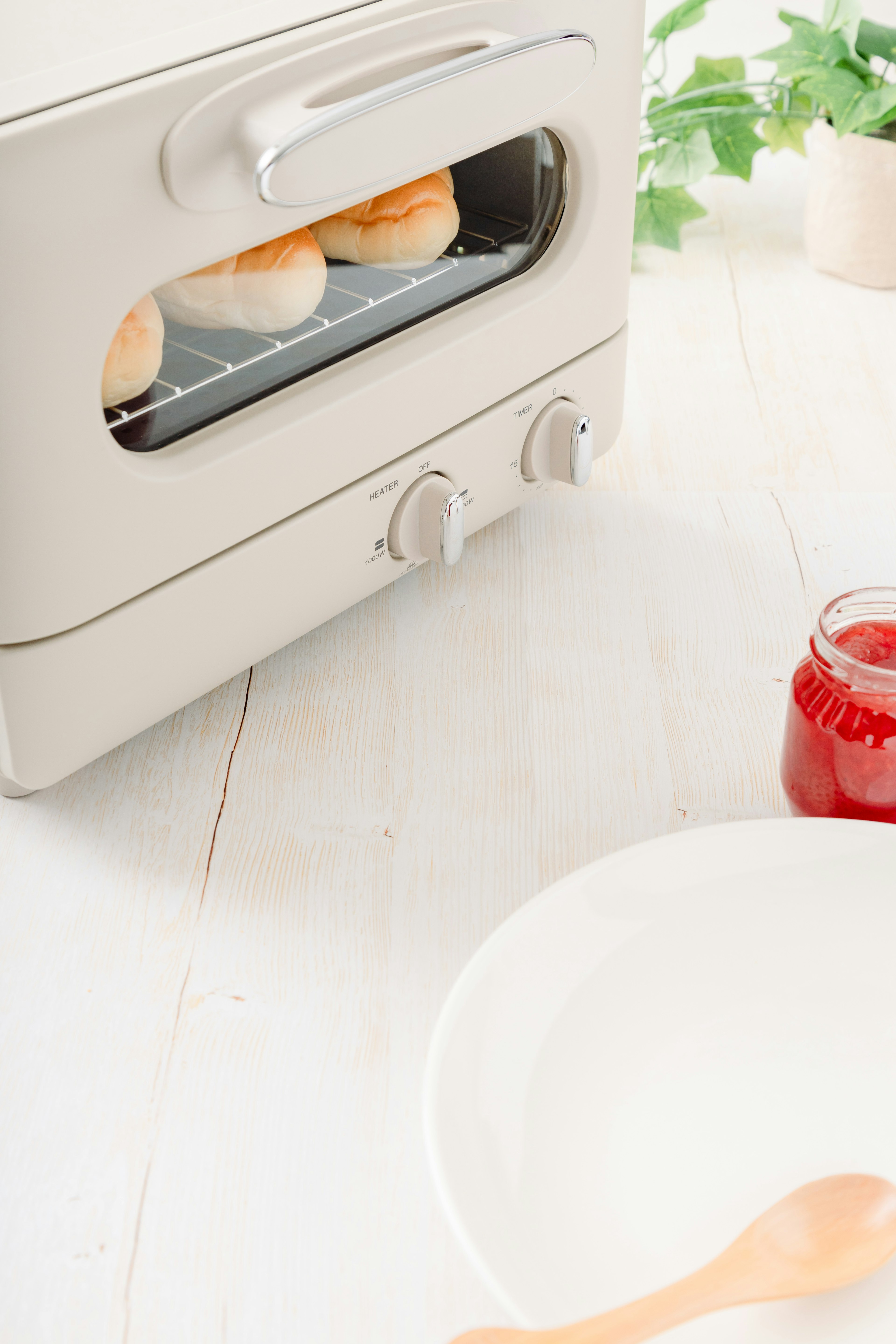 Una escena de cocina con una tostadora blanca y pan tostado junto a un frasco de mermelada roja