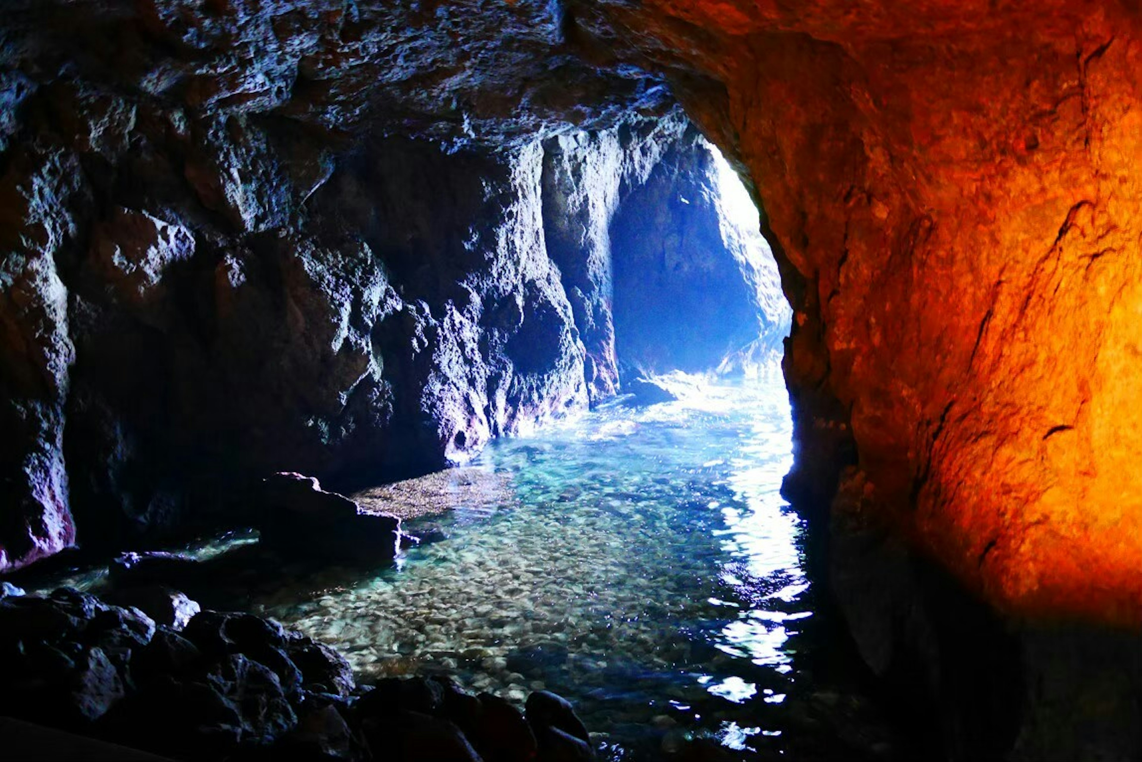 Blick auf das Innere der Höhle mit blauem Wasser und orangefarbenen Felsen