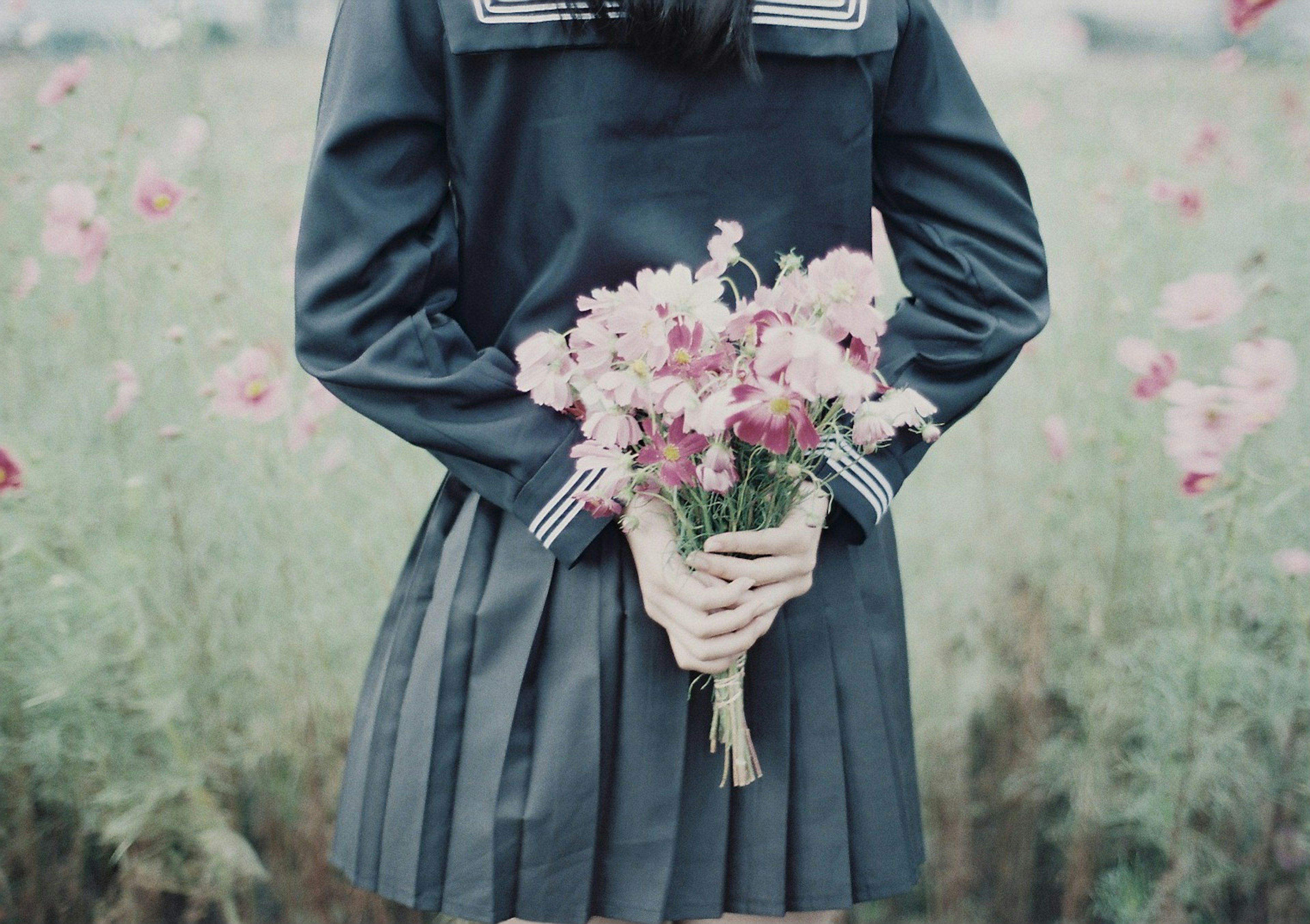 Mädchen mit einem Blumenstrauß in blauer Uniform in einem Blumenfeld