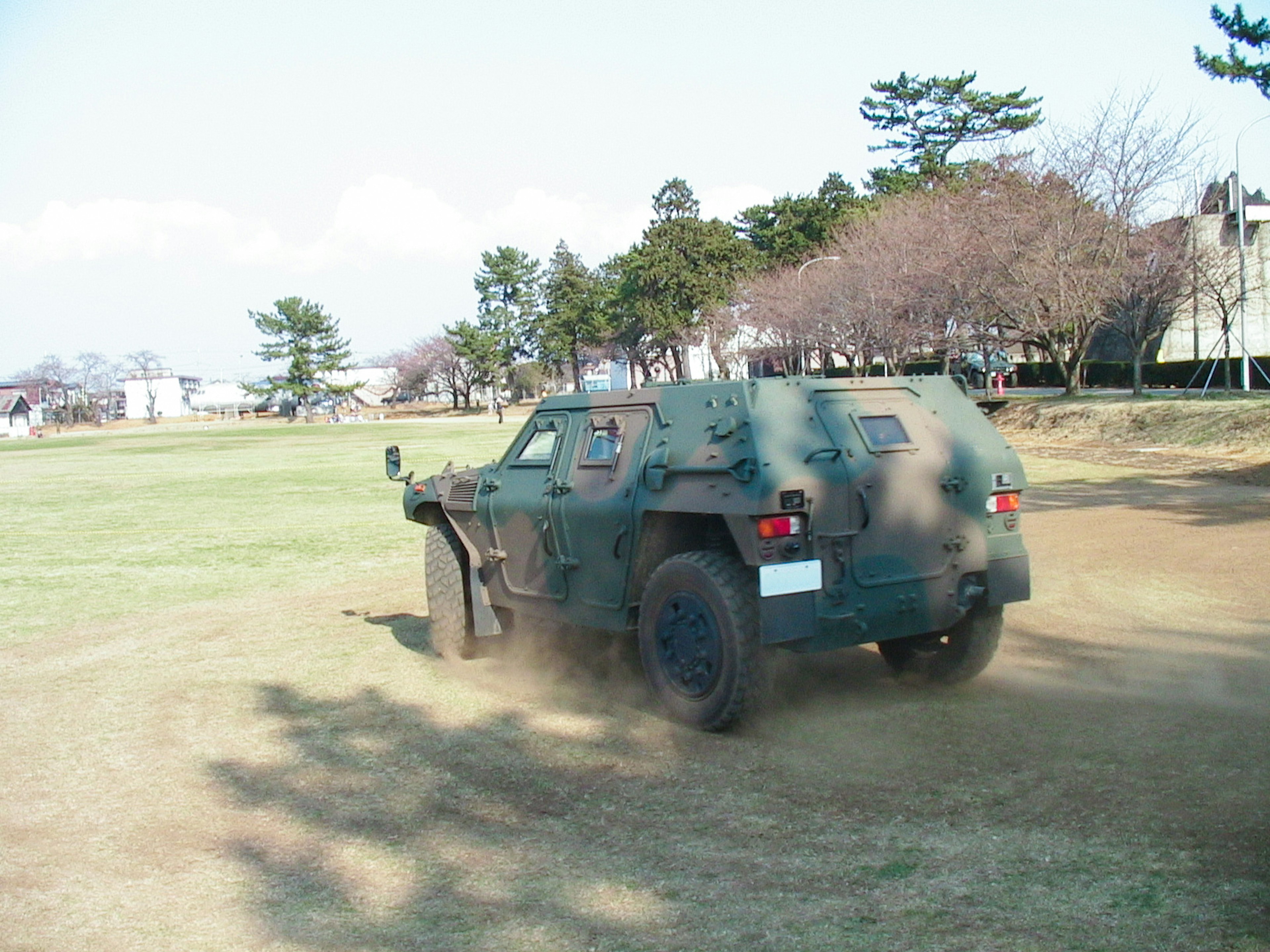 A green armored vehicle driving on dirt with dust clouds