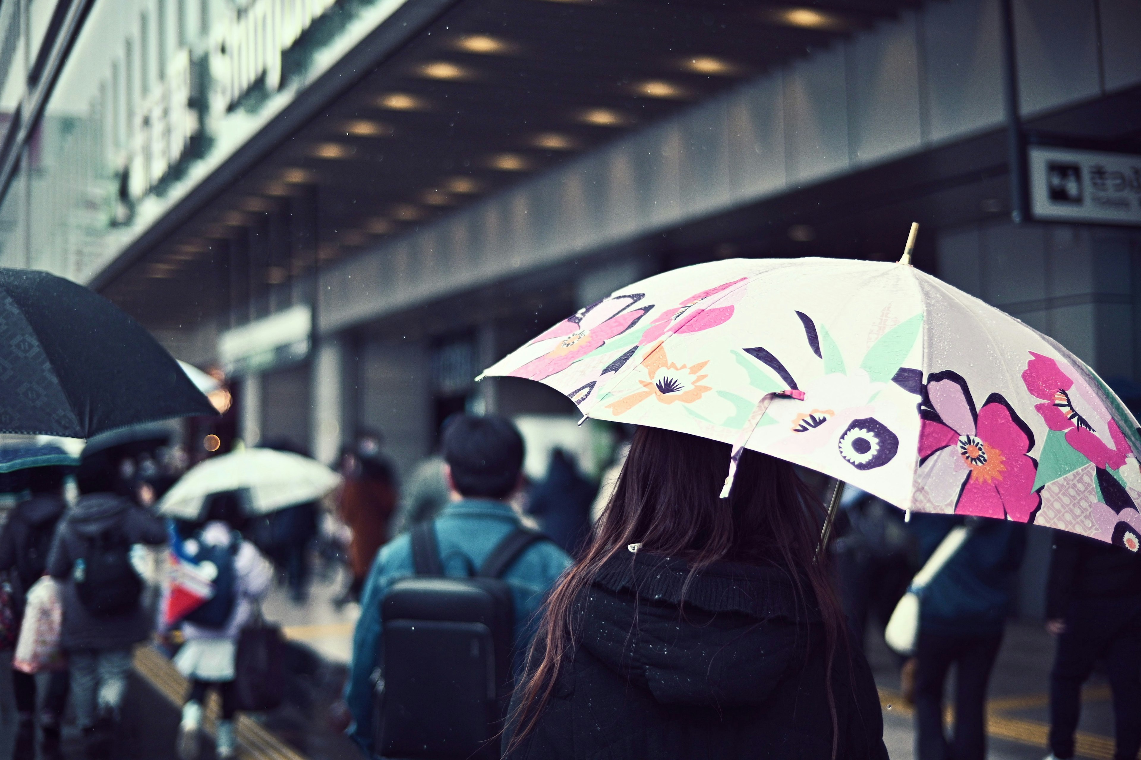 Une femme tenant un parapluie coloré marche sous la pluie avec une foule de personnes et un paysage urbain en arrière-plan