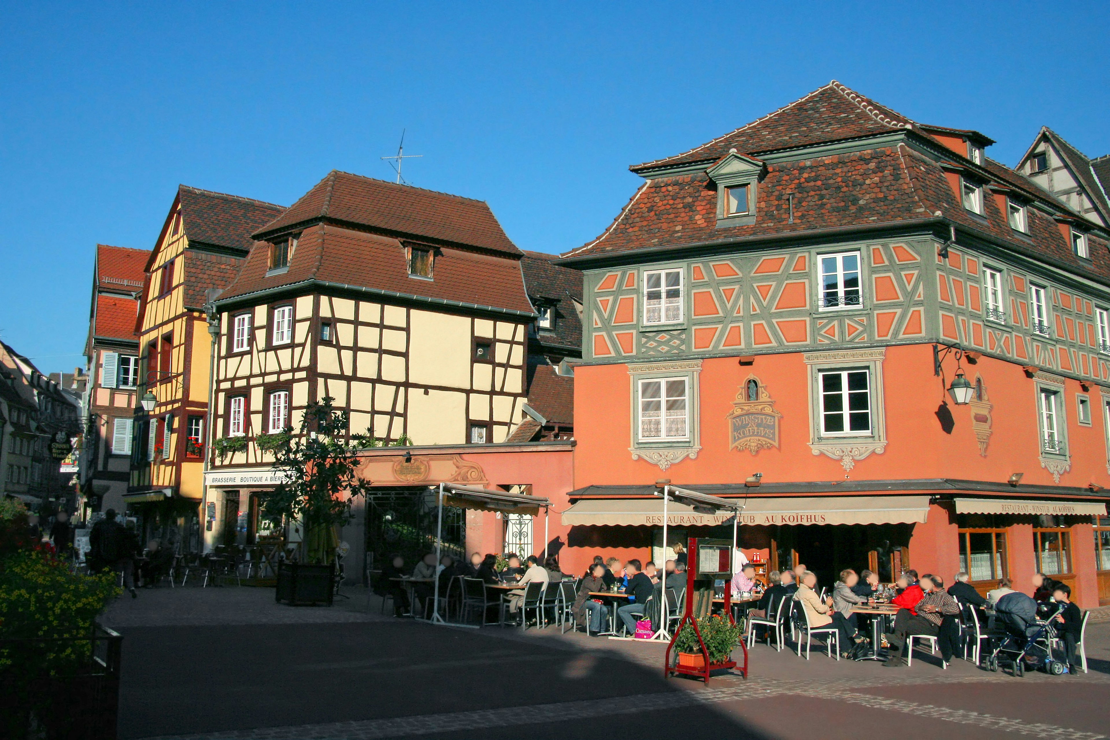 Maisons colorées bordant une place avec des gens assis à des tables en terrasse