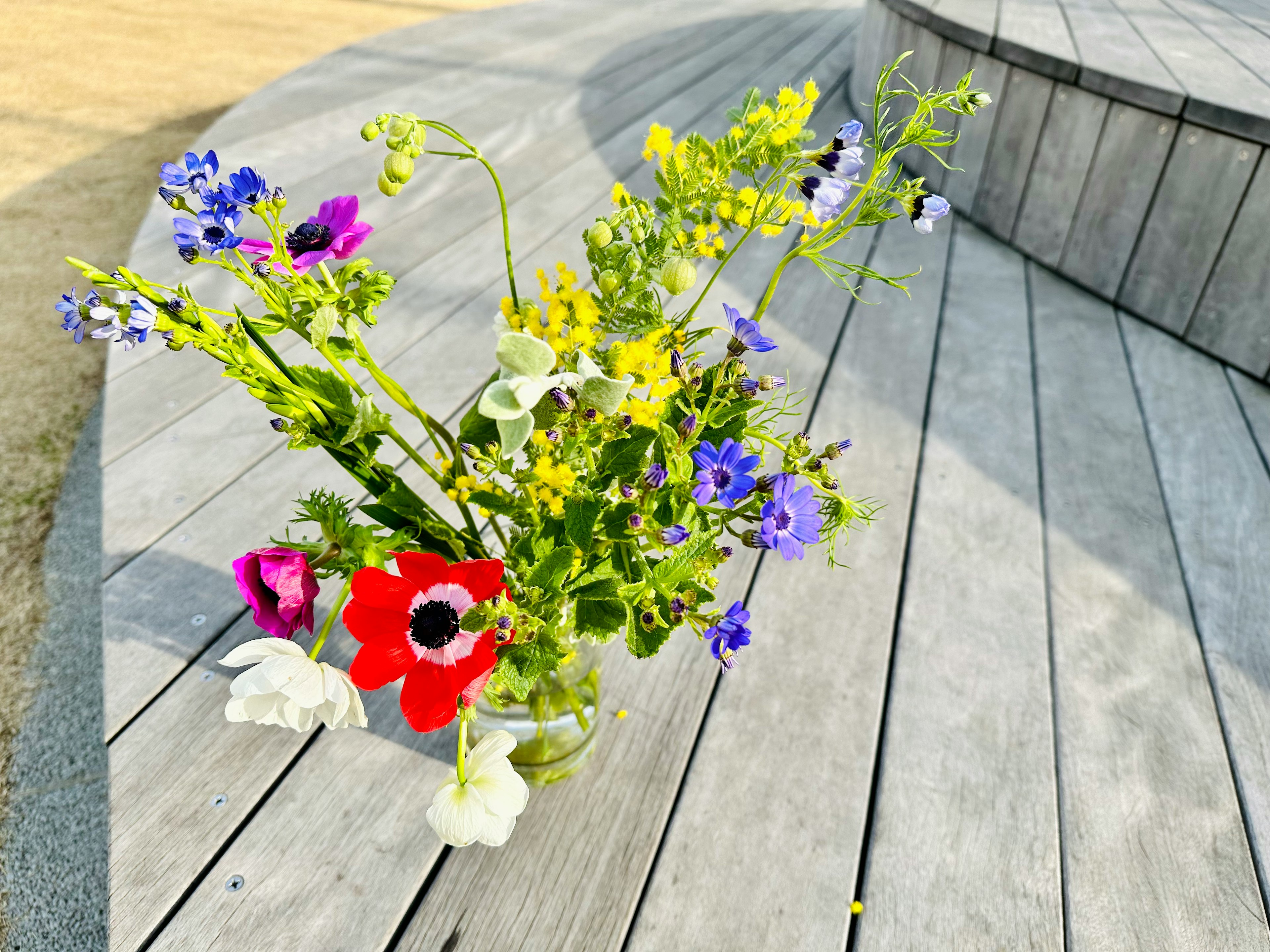 Un vase en verre rempli de fleurs colorées posé sur une scène en bois