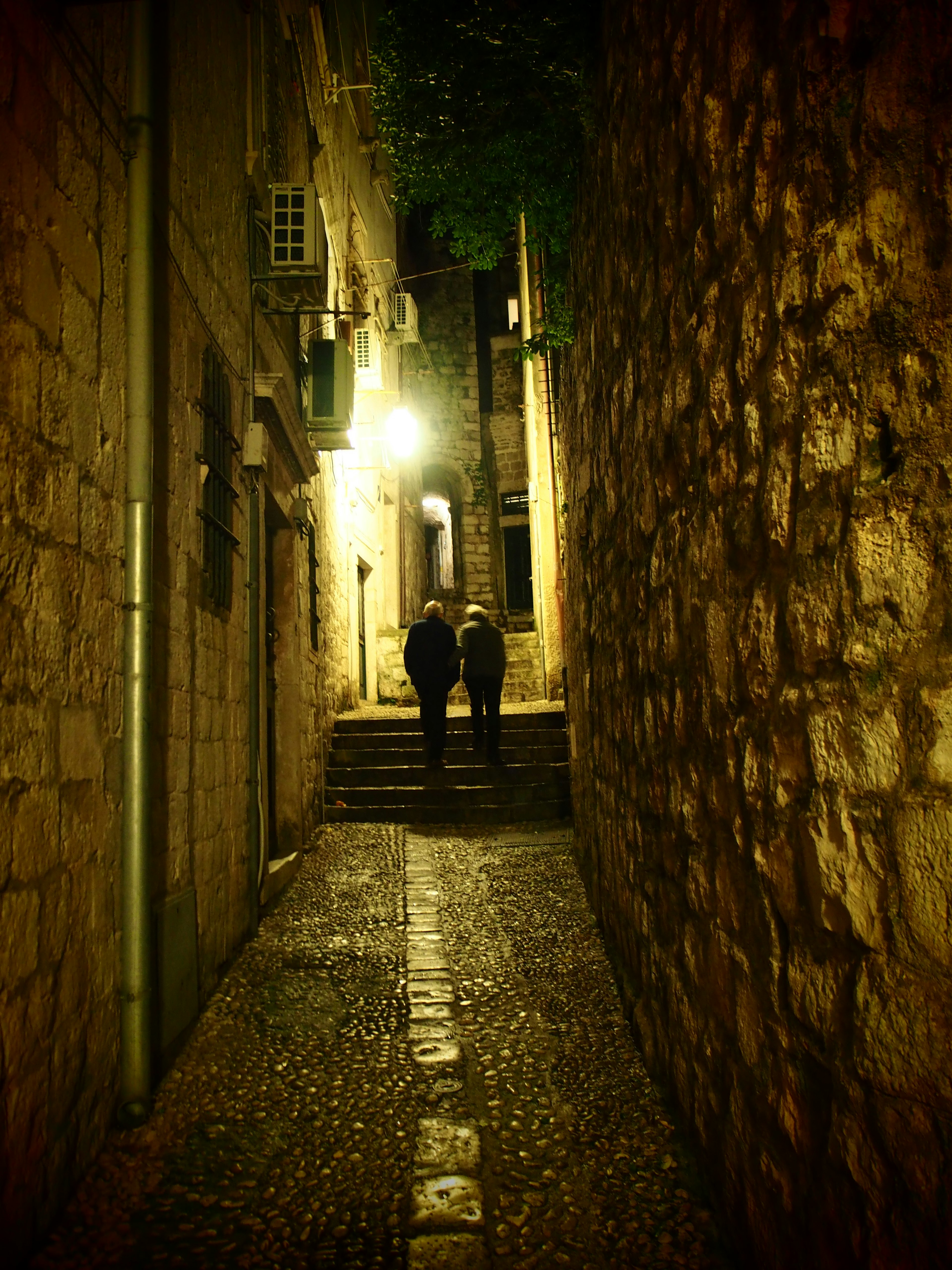 Silhouette de deux personnes dans une ruelle étroite avec des murs en pierre la nuit