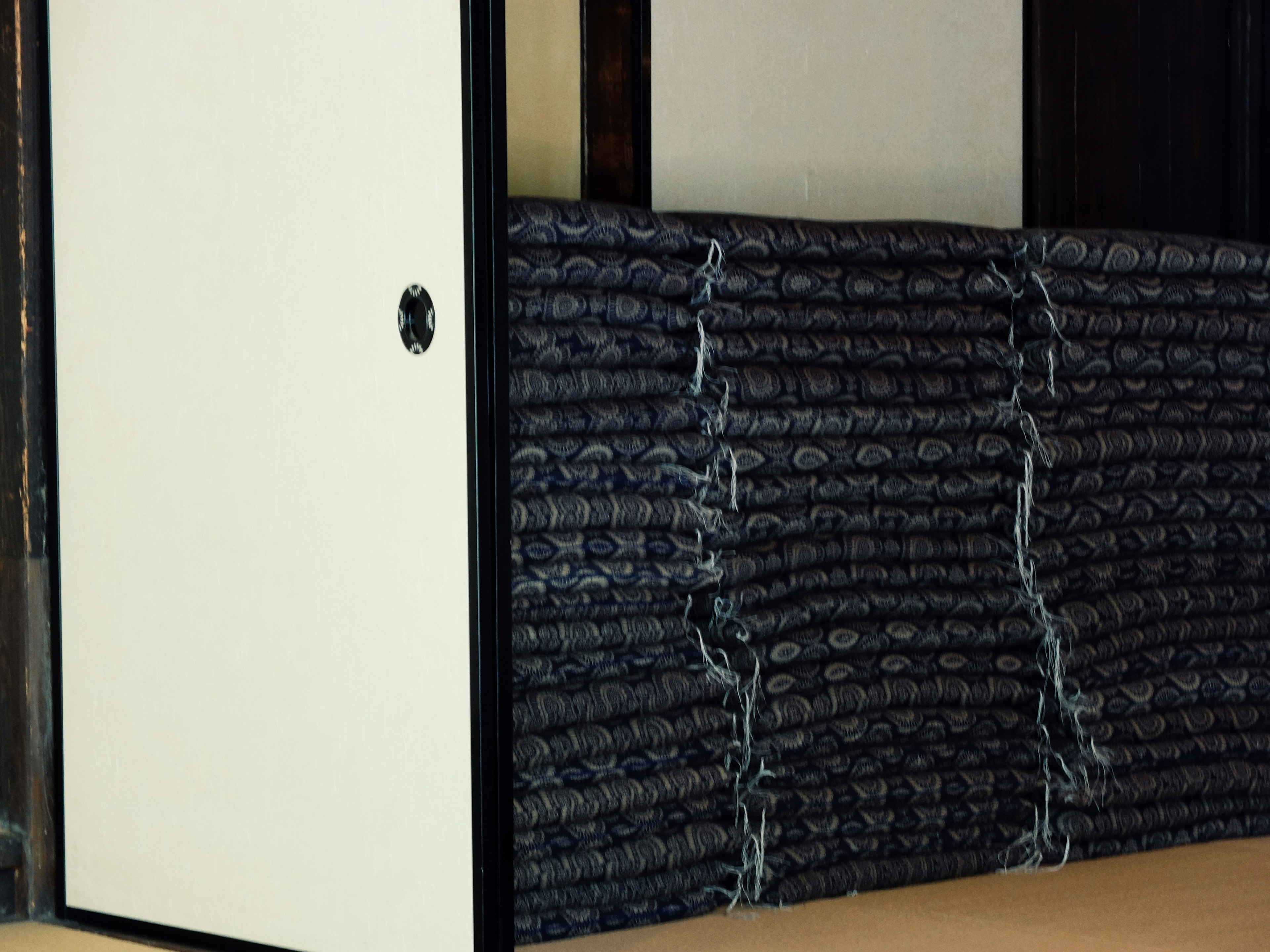 Corner of a Japanese room with stacked black mats and a white door