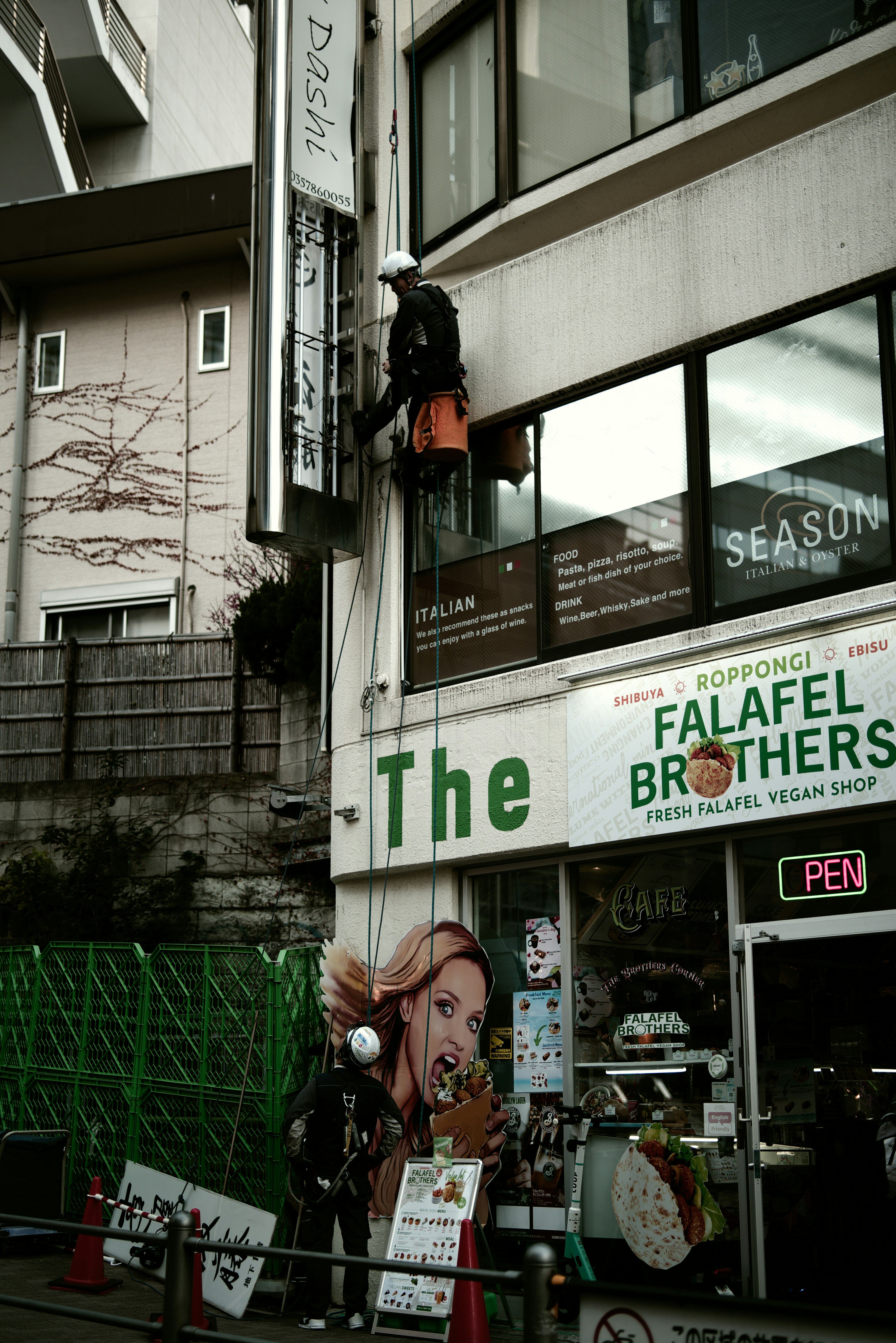 Worker climbing the exterior of a building near a falafel shop sign