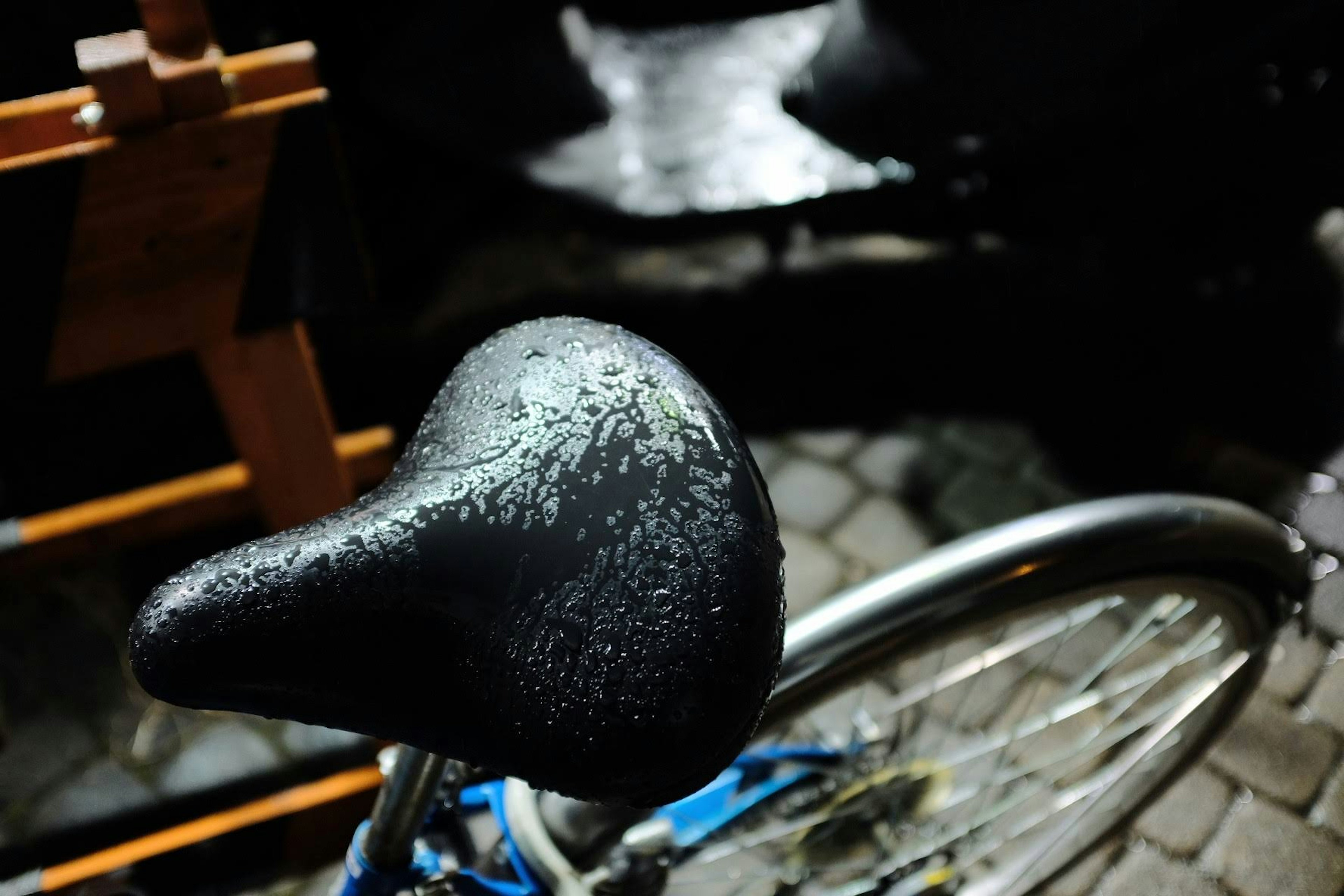 Close-up of a wet bicycle saddle with a blue frame in a nighttime setting